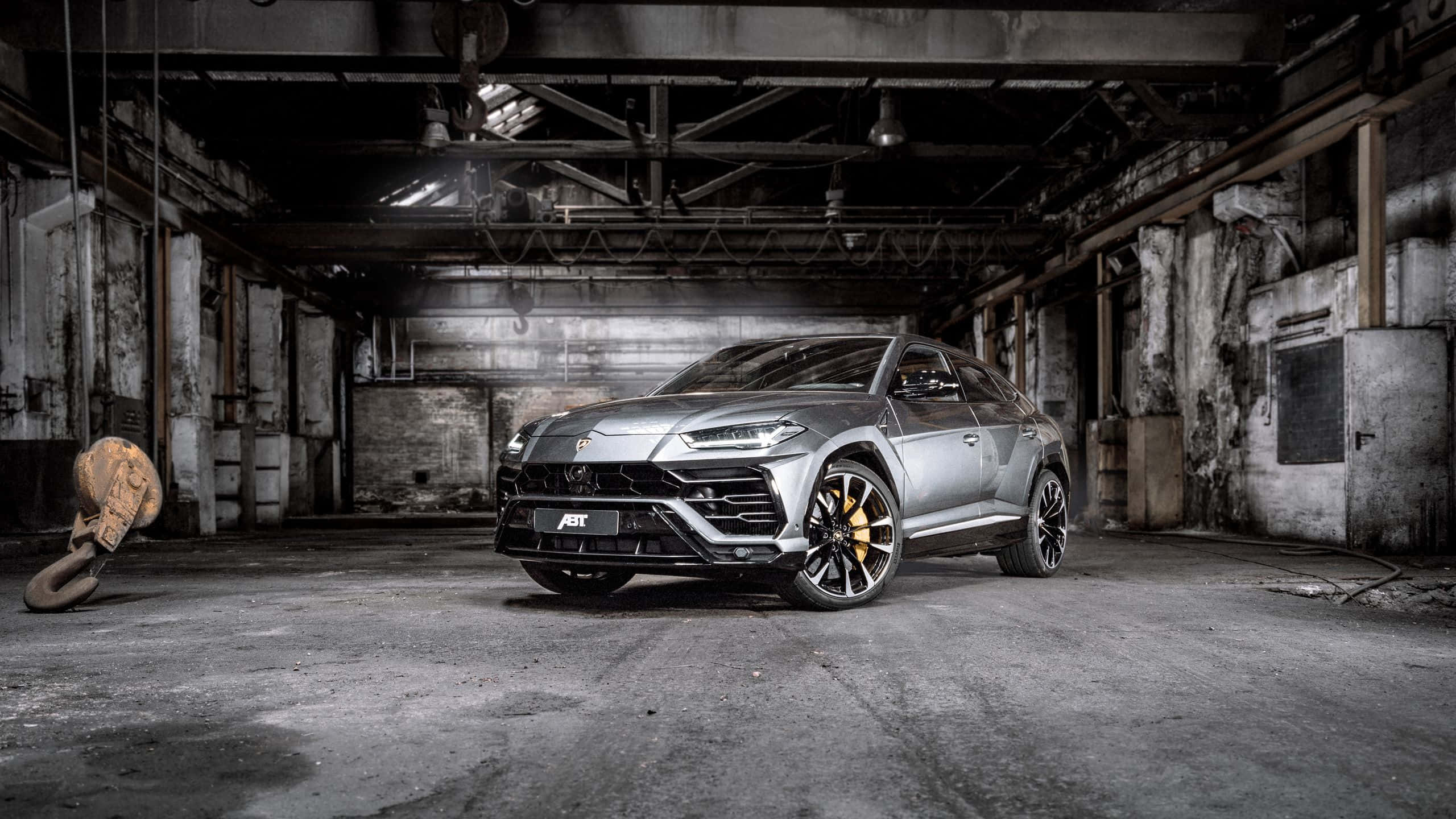 Lamborghini Urus 桌布 壁紙 — 一架時尚的銀色林寶堅尼 Urus 大膽地停放在一個骯髒的廢棄工業倉庫中，倉庫內有裸露的橫樑和混凝土牆。