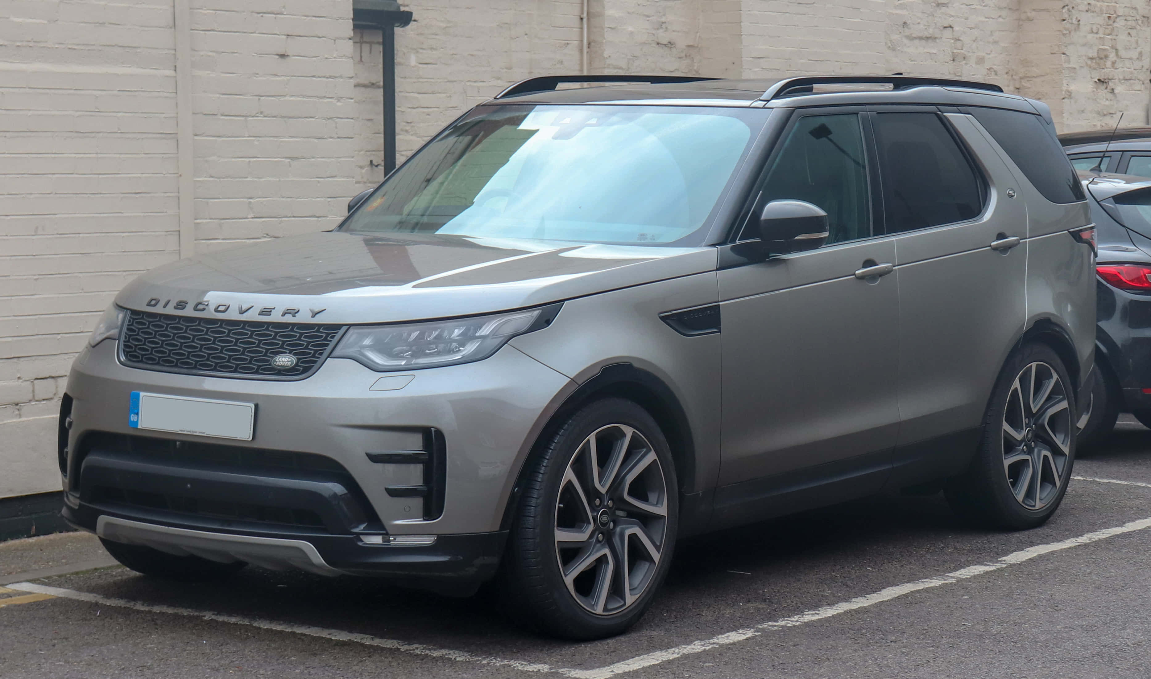 Land Rover Discovery 桌布 壁紙 — 一架時尚的銀色 Land Rover Discovery SUV 停泊在城市地塊旁邊的白色磚牆旁。