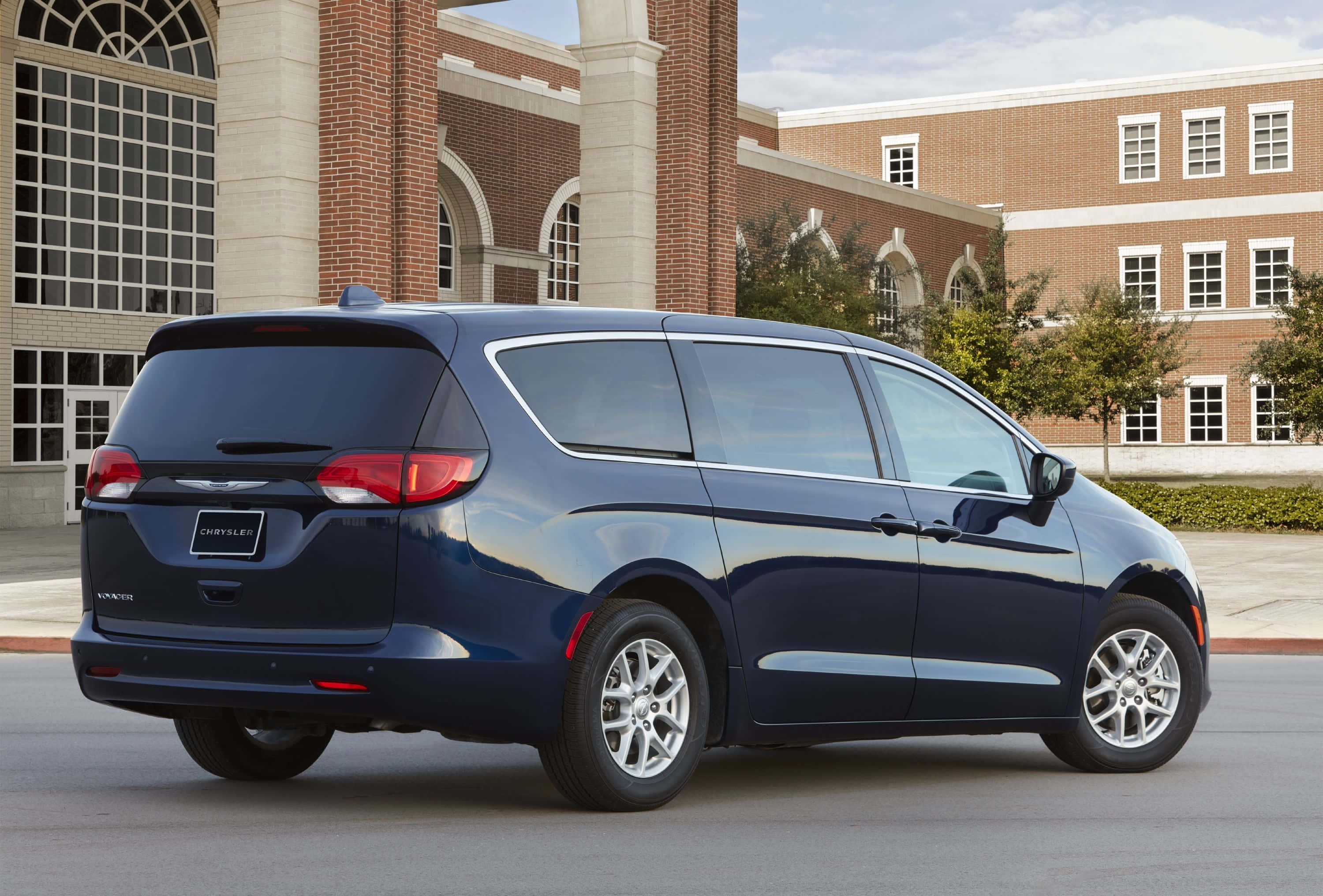 Chrysler Voyager 桌布 壁紙 — 一架時尚的深藍色 Chrysler Pacifica 小型貨車停在有拱形窗戶的磚砌建築前。