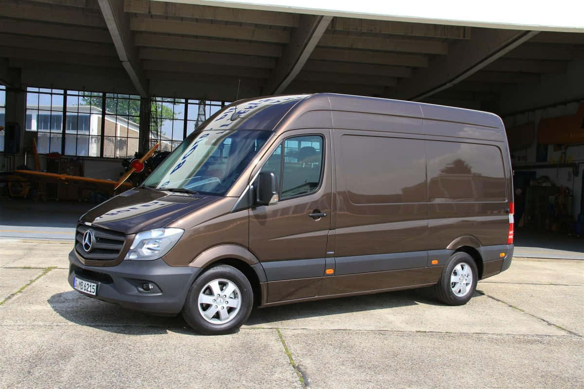 Mercedes Benz Sprinter 桌布 壁紙 — 一架時尚的棕色 Mercedes-Benz Sprinter 客貨車停放在大型工業機庫下，陽光透過窗戶照射進來。