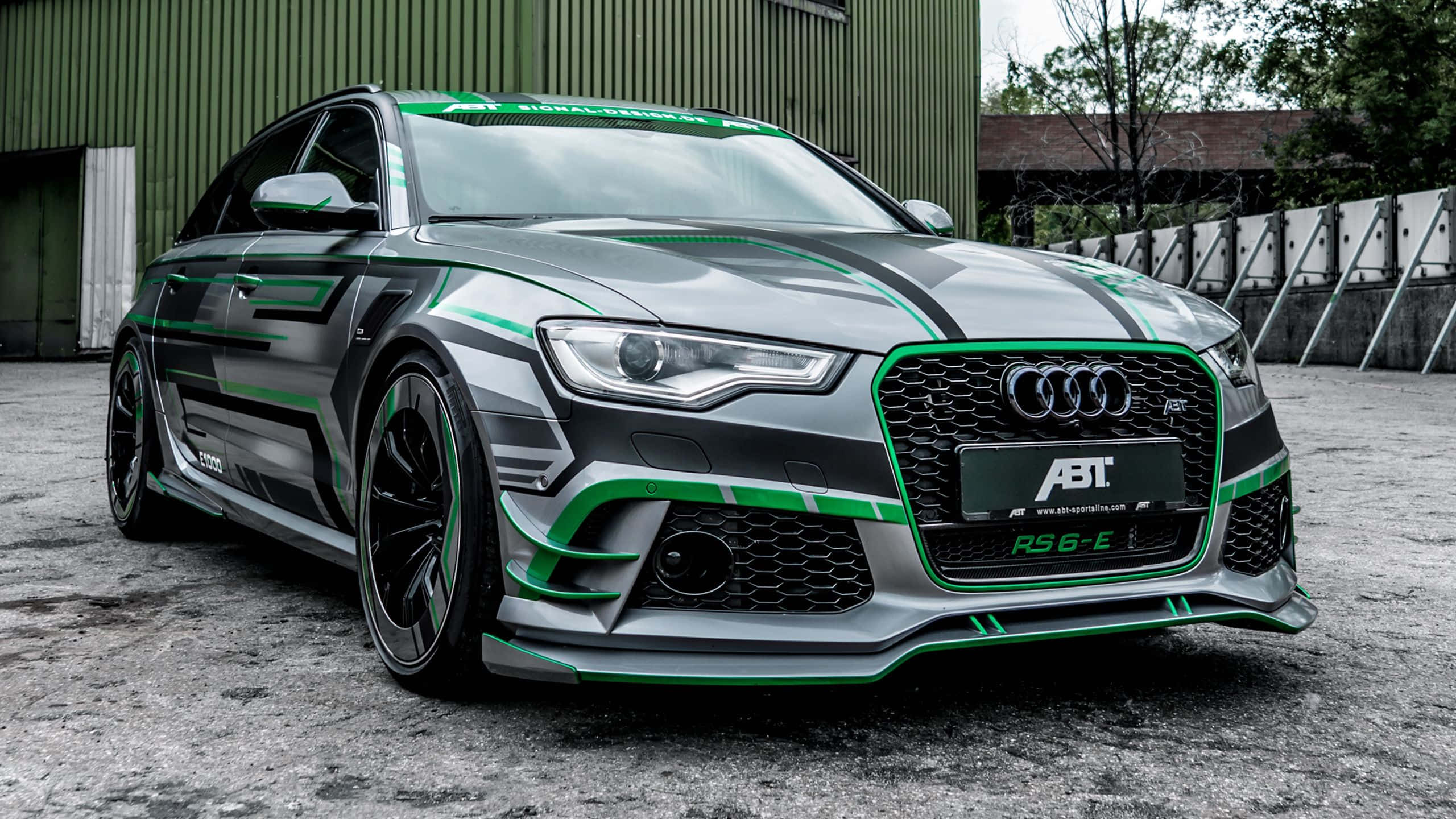 Audi Rs6 桌布 壁紙 — 一架時尚的灰色Audi RS6-E，帶有醒目的綠色賽車條紋，停在綠色工業建築前。