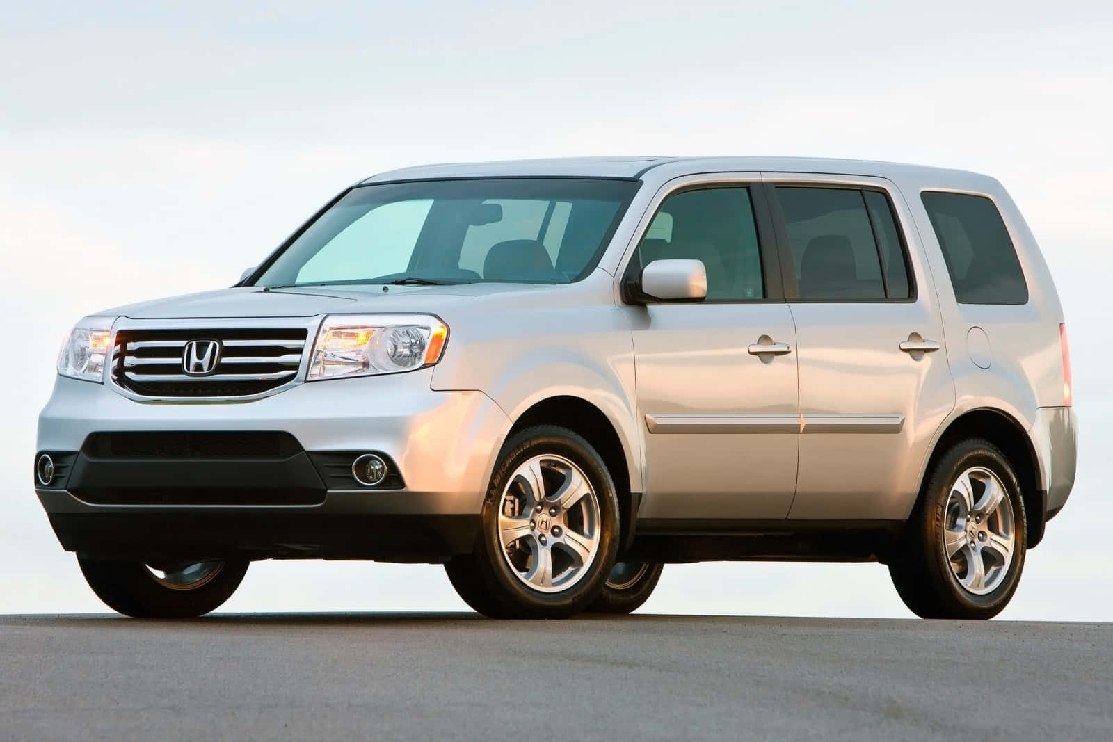 Honda Pilot 桌布 壁紙 — 一架時尚的銀色本田Pilot SUV停在平坦表面上，柔和日光下，背景是晴朗天空。