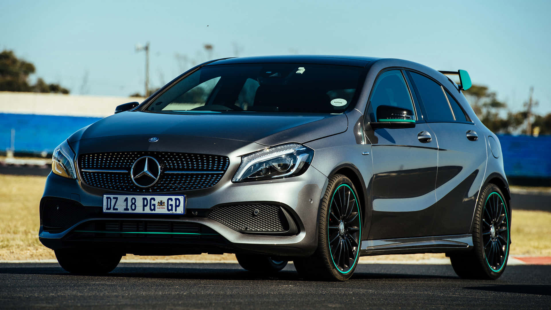 Mercedes Benz A-class 桌布 壁紙 — 一架時尚的銀色 Mercedes-AMG A45 S 跑車，配備綠色點綴的輪圈，停在瀝青賽道上，天空湛藍。
