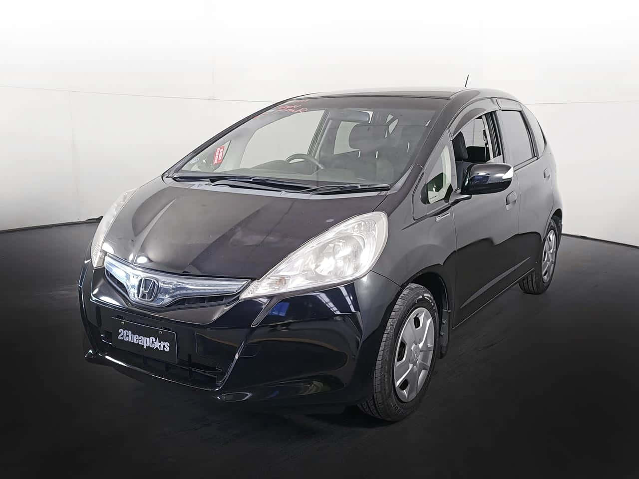 Honda Fit 桌布 壁紙 — 一架時尚黑色本田 Fit 停泊在室內深色地板上，背景是純白牆壁。