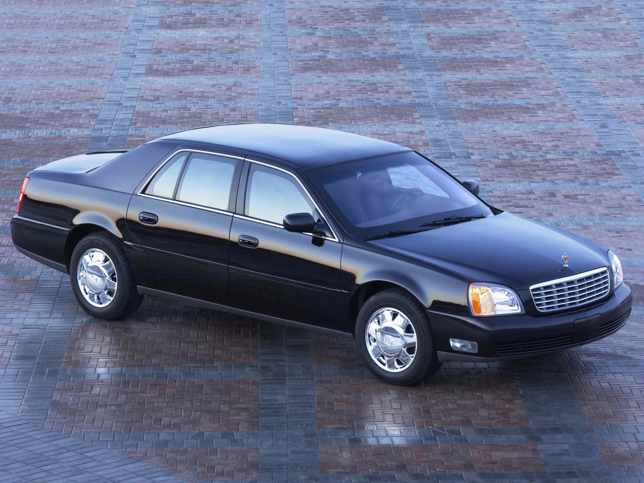Cadillac Deville 桌布 壁紙 — 一架時尚黑色豪華轎車停泊在圖案磚砌廣場上，沐浴在明亮日光下。