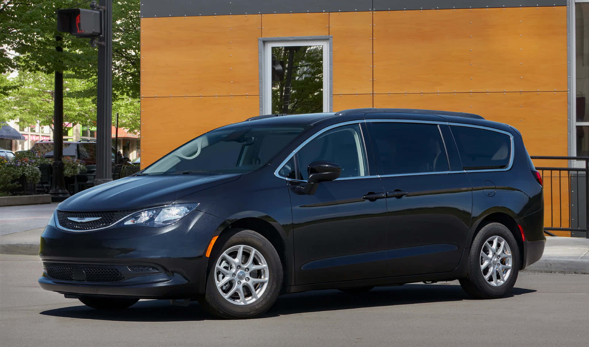 Chrysler Voyager 桌布 壁紙 — 一架時尚黑色小型貨車停泊在陽光明媚的城市街道上，旁邊是一座現代木結構建築。