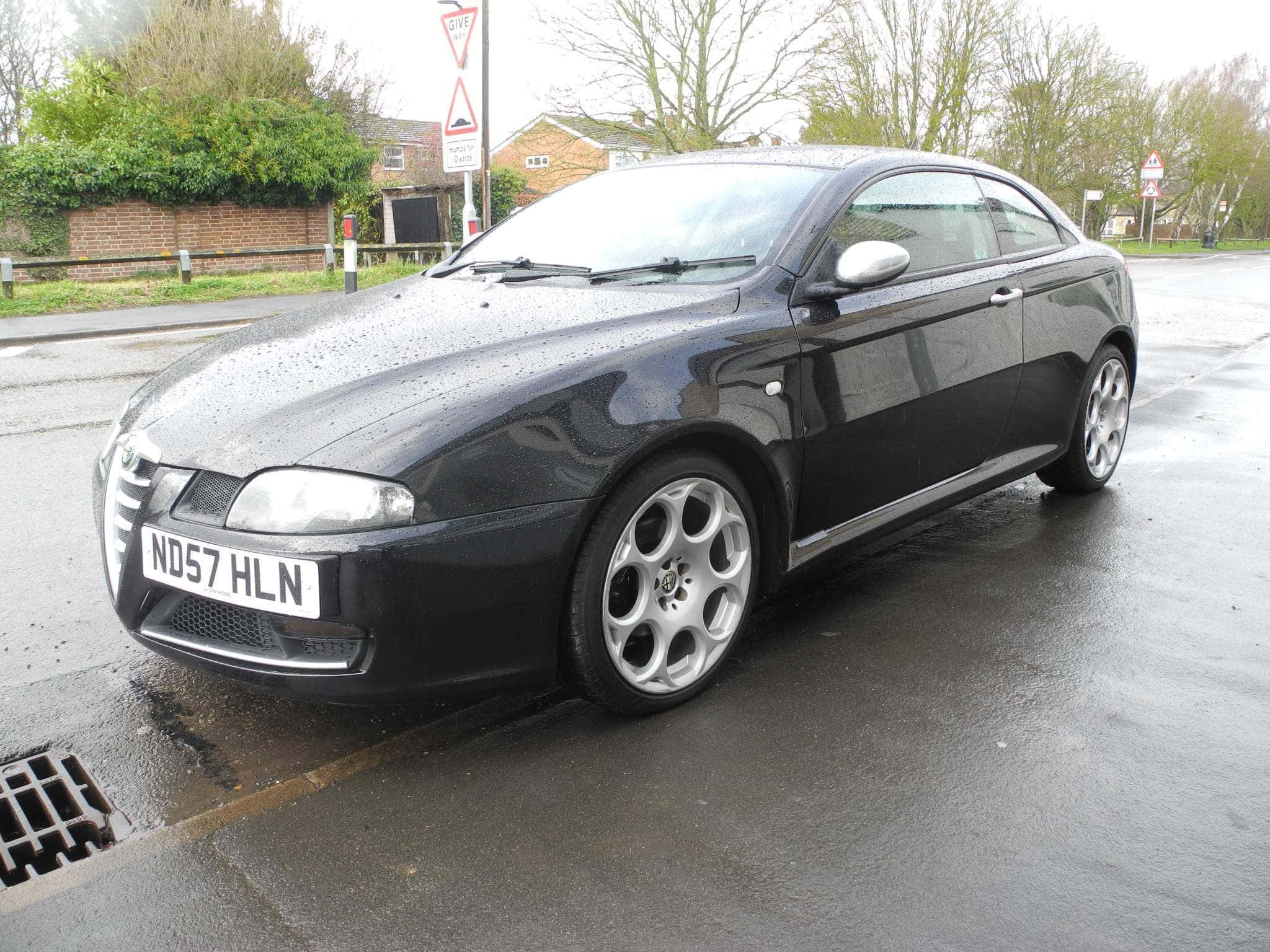 Alfa Romeo Gt 桌布 壁紙 — 一架時尚的黑色愛快羅密歐轎跑車停在潮濕的住宅街道上，天空多雲。