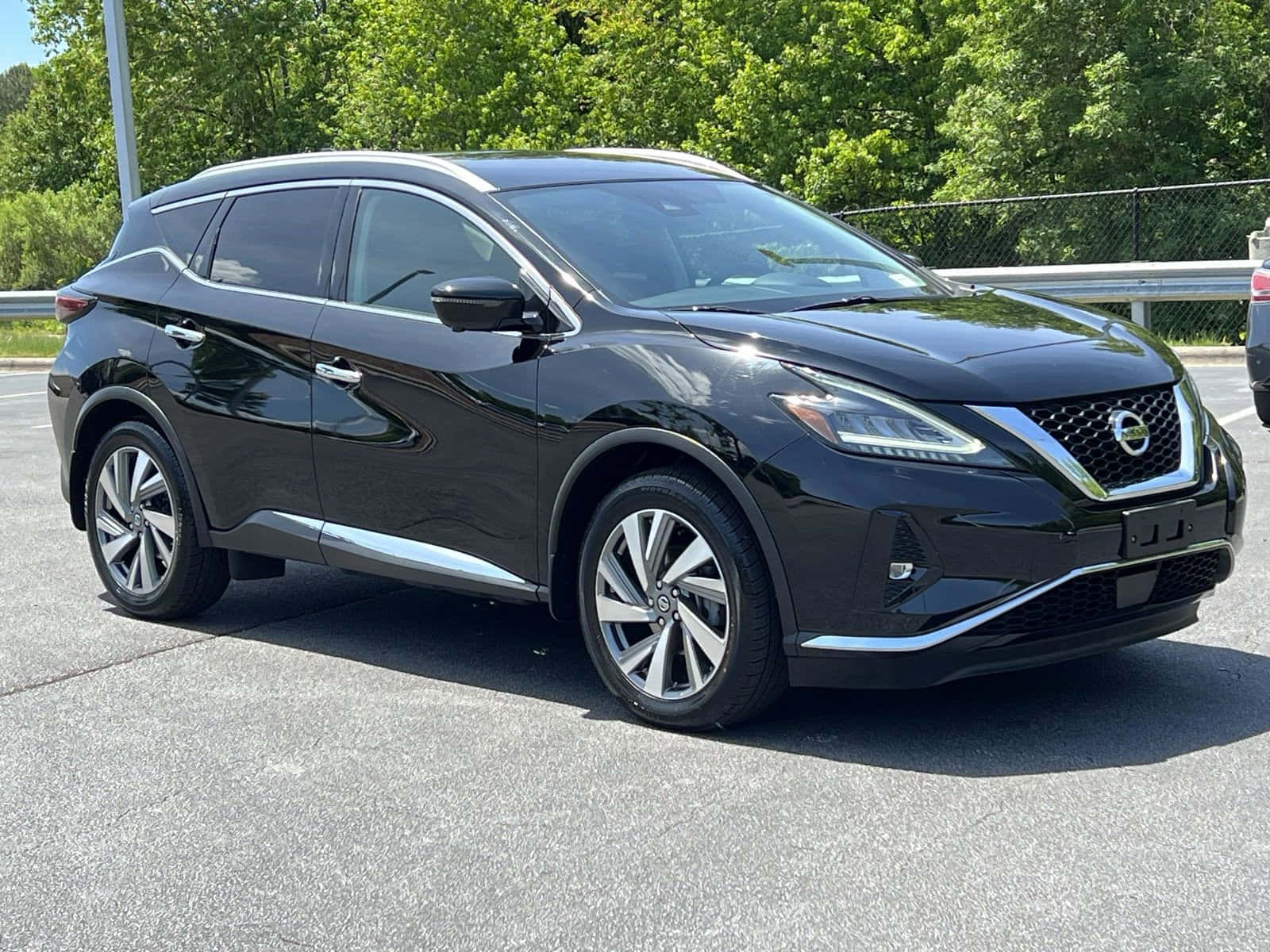 Nissan Murano 桌布 壁紙 — 一架時尚的黑色日產Murano SUV在明亮的陽光下停在瀝青路上，背景是茂密的綠樹。