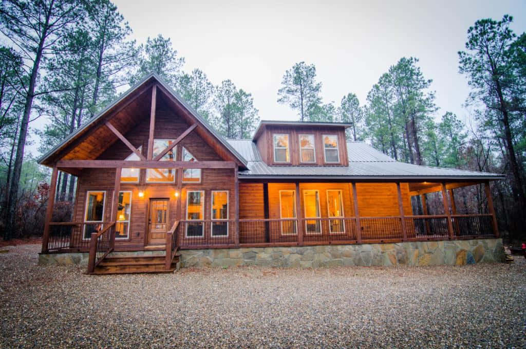 Fall Cabin 桌布 壁紙 — 一間舒適的木屋，帶有溫暖發光的窗戶，坐落在黃昏時分高大的松樹之間。