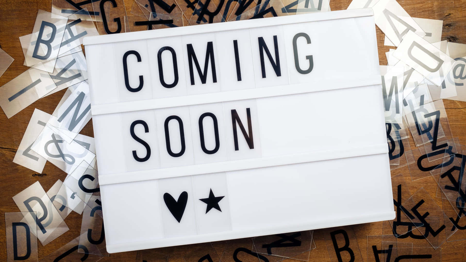 白色燈箱帶有「COMING SOON」和符號，周圍散落字母瓷磚在木頭上。