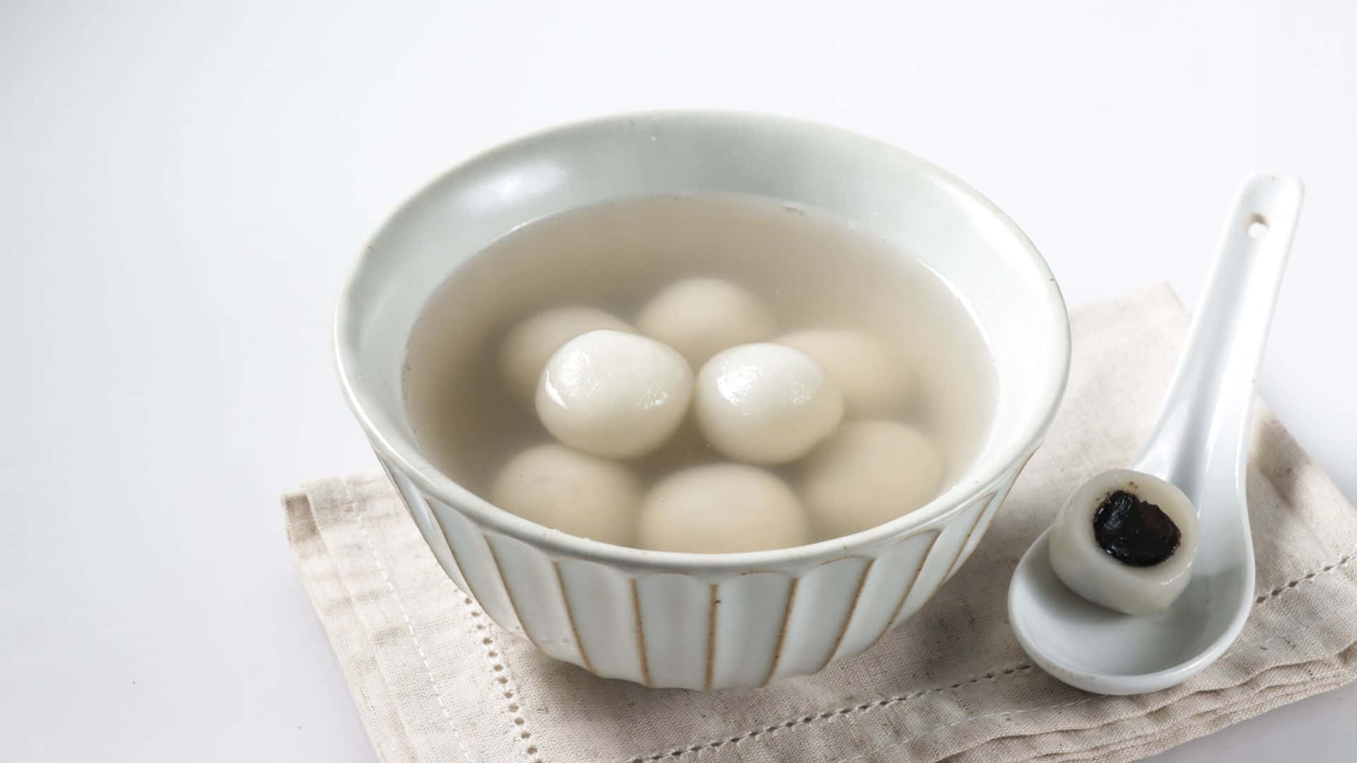  壁紙 — 一個白色陶瓷碗盛載著冒煙的甜湯圓，放在清湯中，旁邊有一隻裝著深色餡料的湯匙。