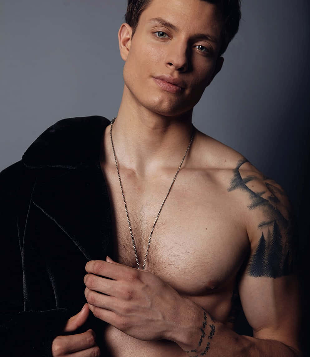 Matt Rife 桌布 壁紙 — 一個赤裸上身、有紋身、穿著天鵝絨外套的男人，在深灰色工作室背景前自信地擺姿勢。