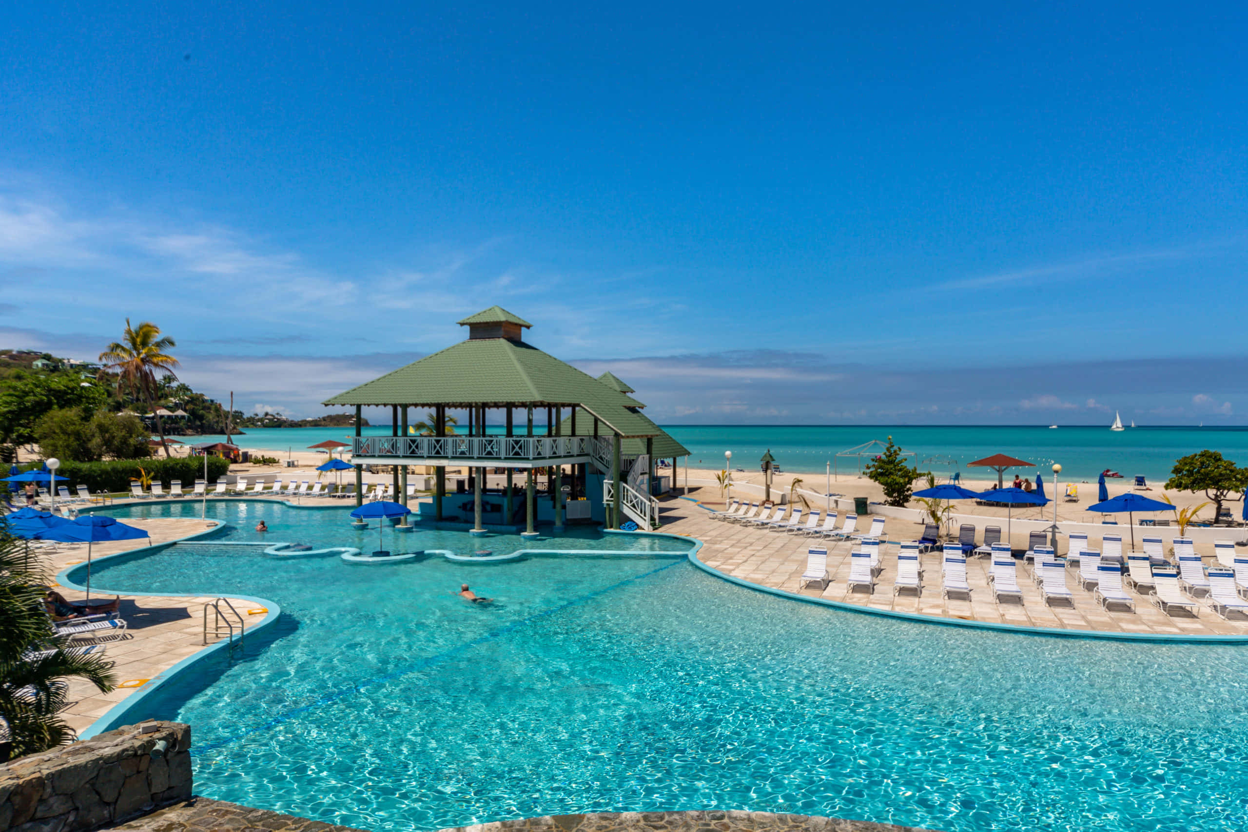 Beach Resort 桌布 壁紙 — 一個充滿活力的藍綠色泳池，配有一個綠色屋頂的涼亭，俯瞰著沙灘和寧靜的海洋，在清澈的藍天下。