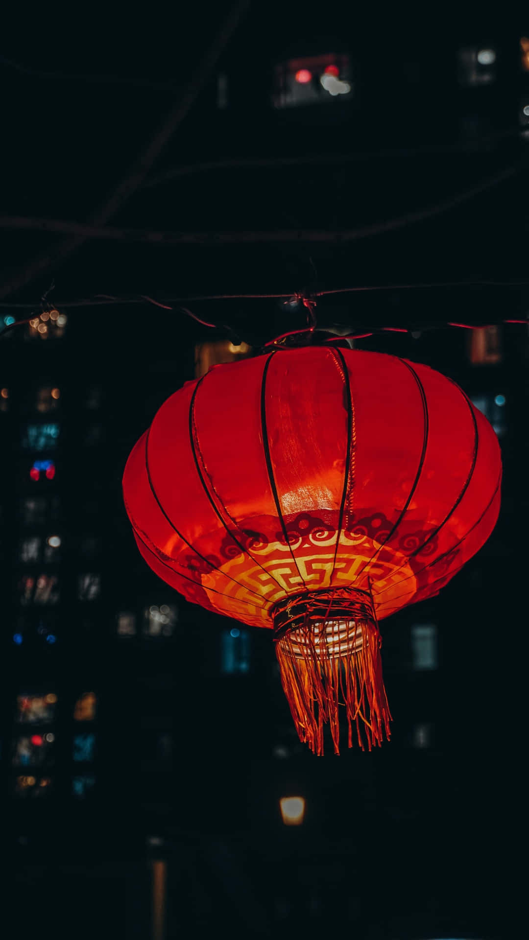  壁紙 — 一個發光的紅色紙燈籠，帶有精緻圖案，懸掛在夜晚黑暗的城市景觀中。