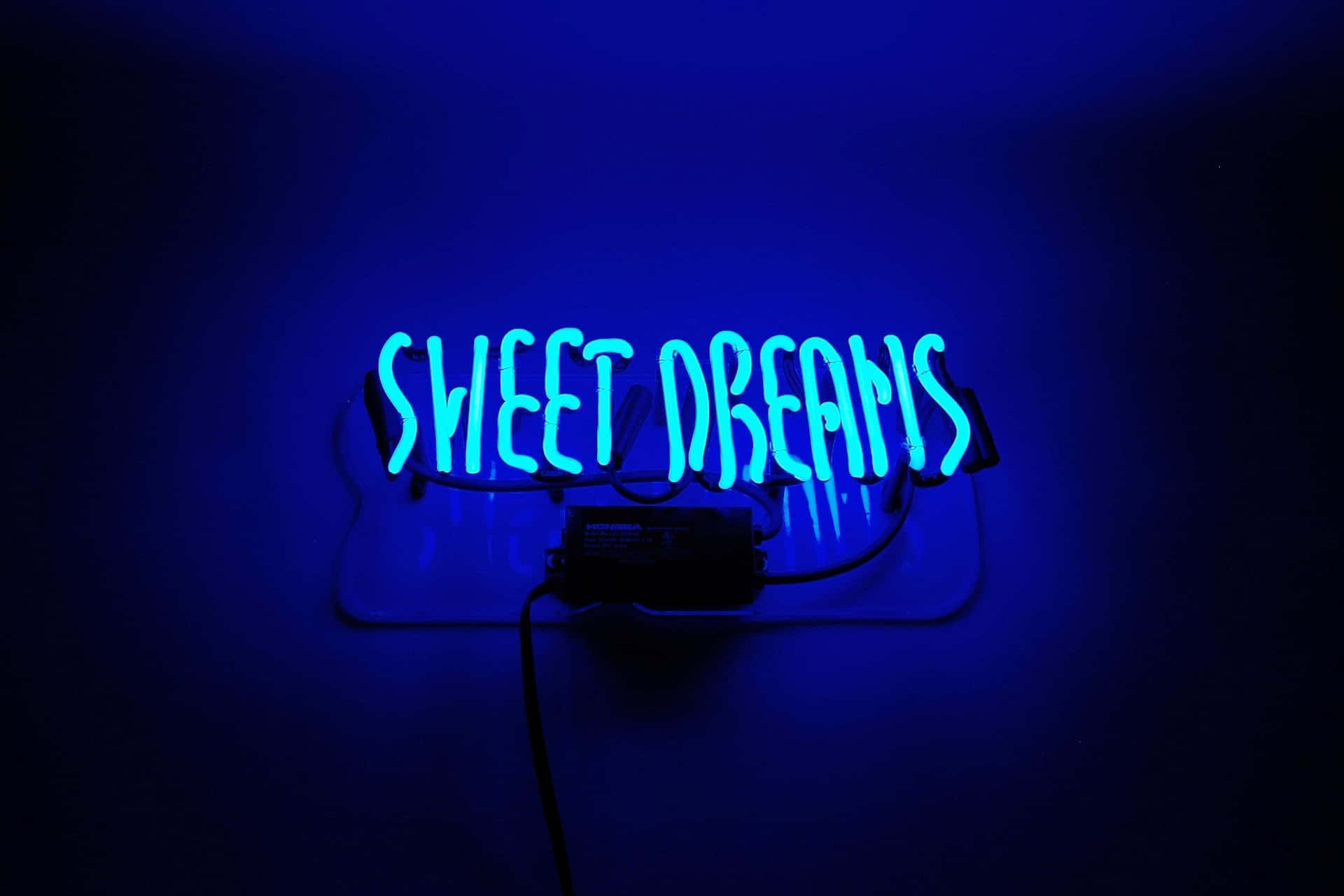  壁紙 — 一個發光的藍色霓虹燈牌，上面寫著 sweet dreams，在昏暗的房間中向深色牆壁投射出柔和的光線。