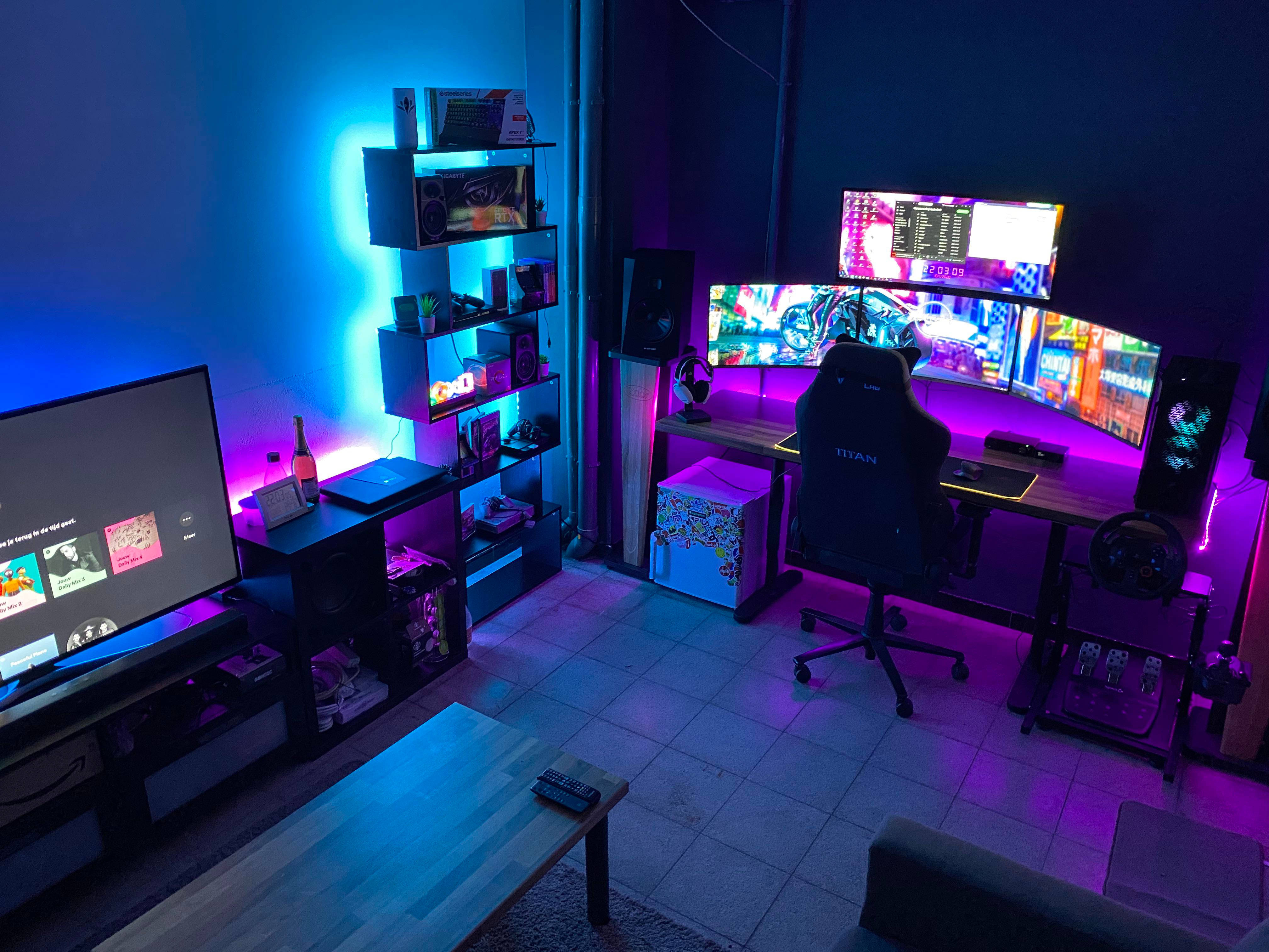 遊戲房間桌面與電視 壁紙 — 一個光線昏暗的遊戲室，沐浴在藍色和紫色的LED燈光中，配備曲面顯示器和Titan椅子。