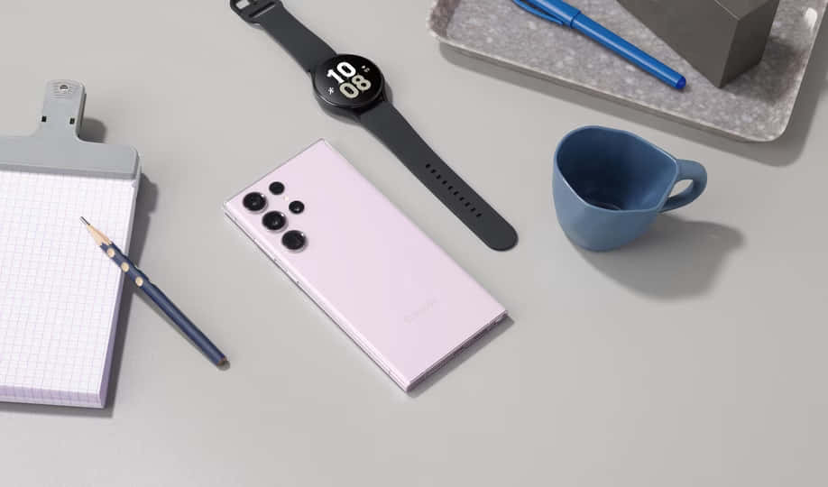 Samsung S23 Ultra 桌布 壁紙 — 一個極簡風格的平鋪構圖，包含薰衣草色智能手機、黑色智能手錶、藍色馬克杯和文具，放置在灰色表面上。