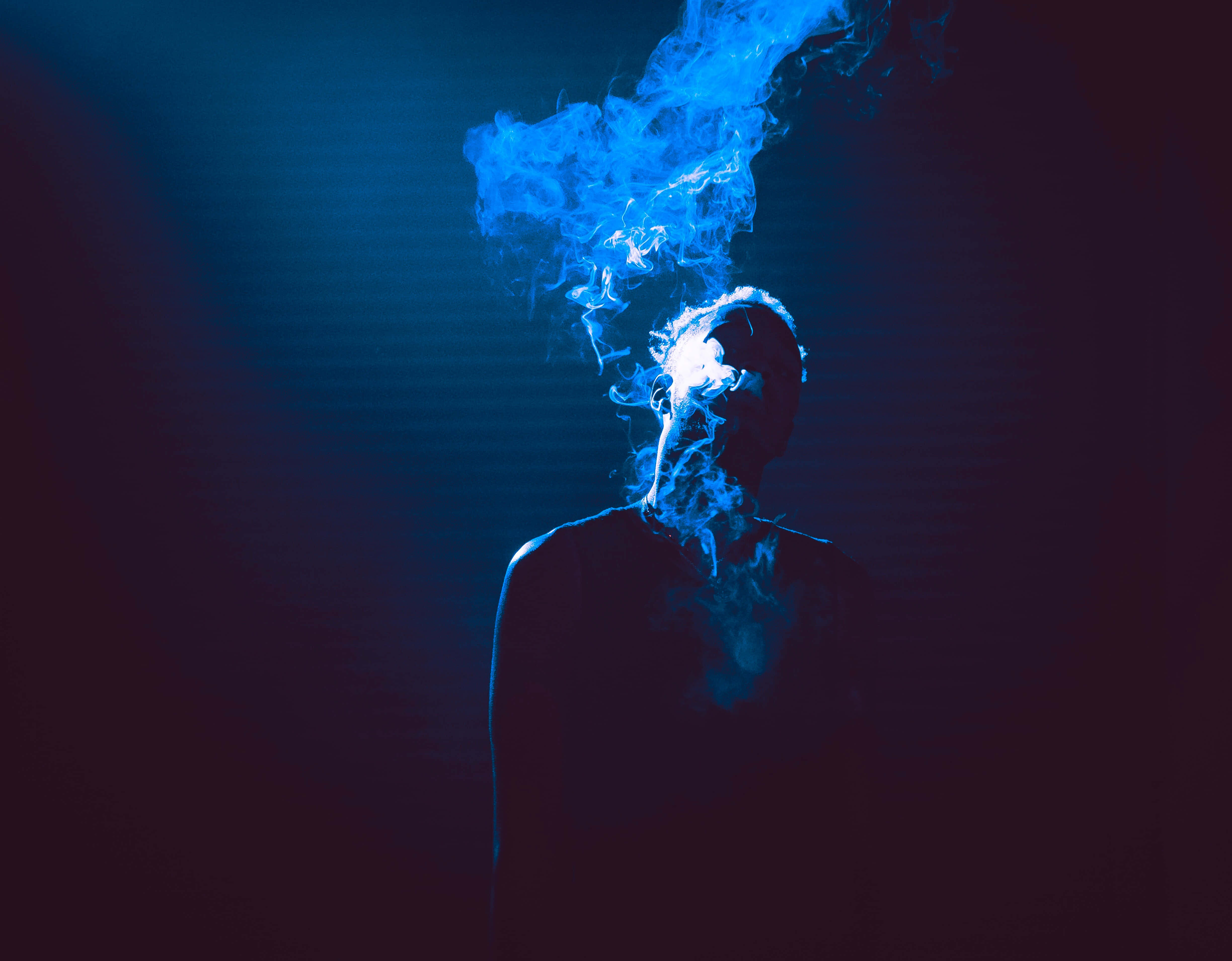 Smoke Blue 桌布 壁紙 — 一個剪影人物在深色漸變背景上呼出充滿活力的藍色煙霧。