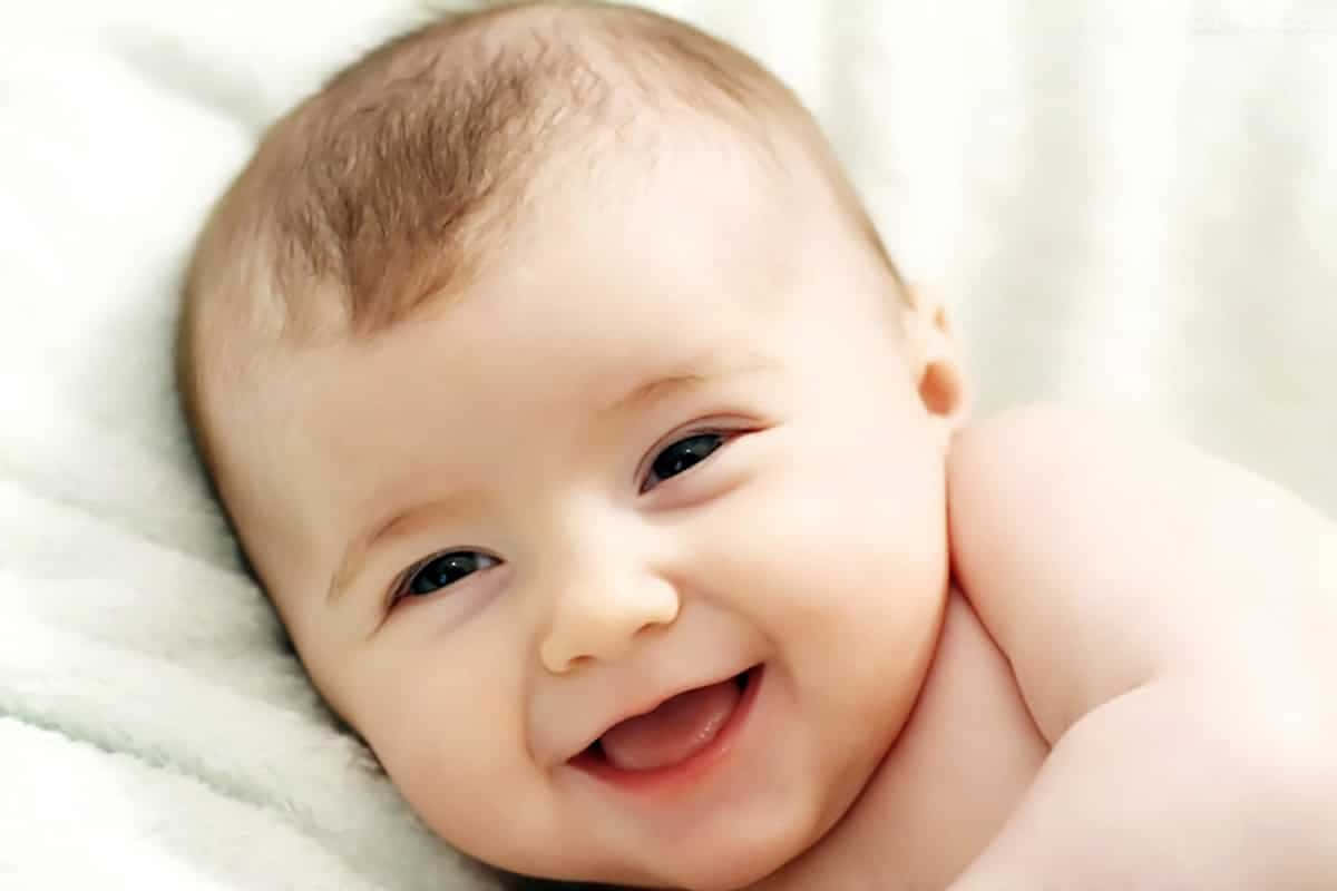  壁紙 — 一個快樂的嬰兒，深色眼睛和柔軟的棕色頭髮，躺在蓬鬆的白色毯子上，開懷大笑。