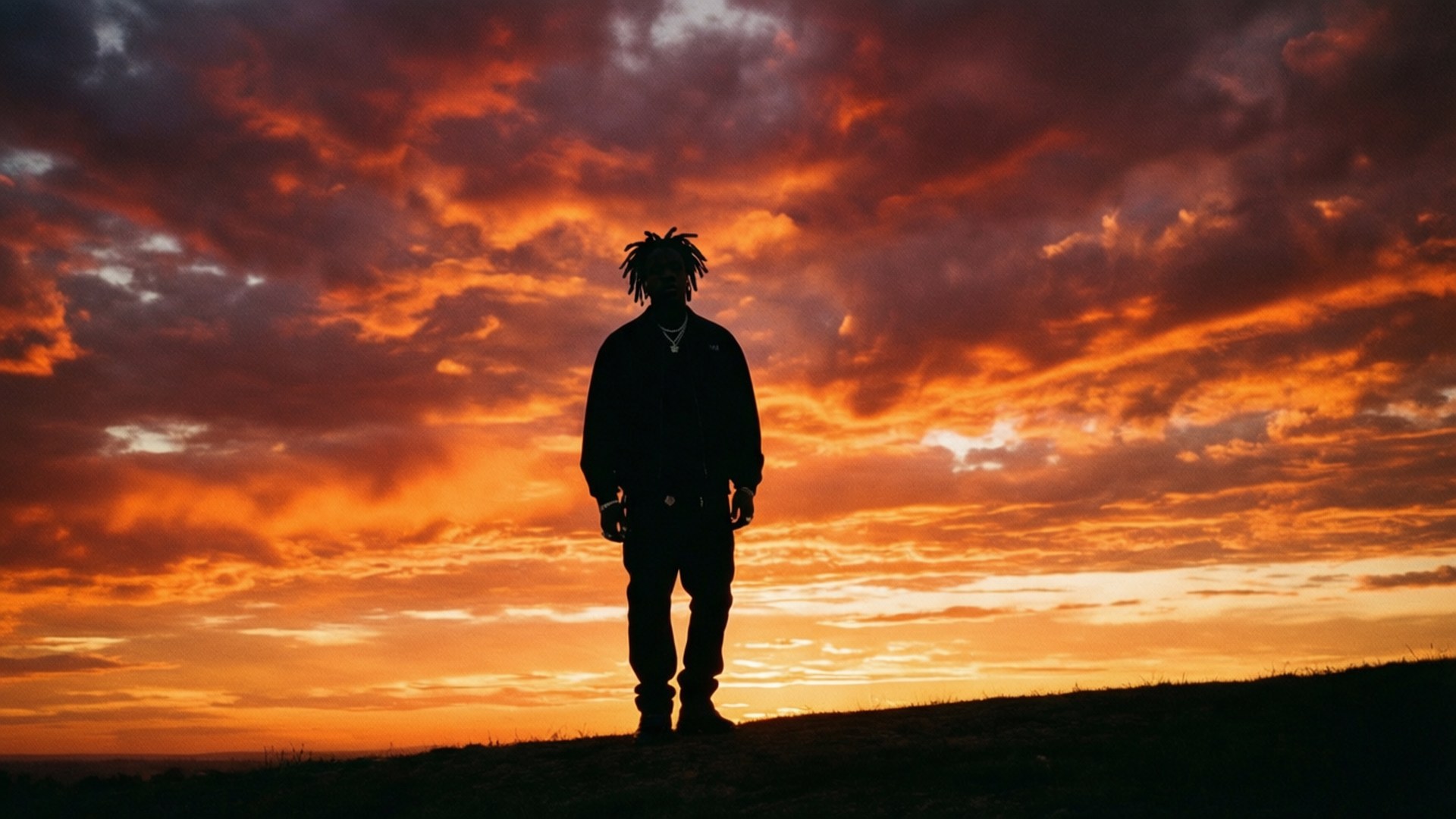 Sunset Silhouette 壁紙 — 一個留著辮子的人的孤獨剪影，站在長滿草的山丘上，背景是火紅的橙色和紅色日落天空。