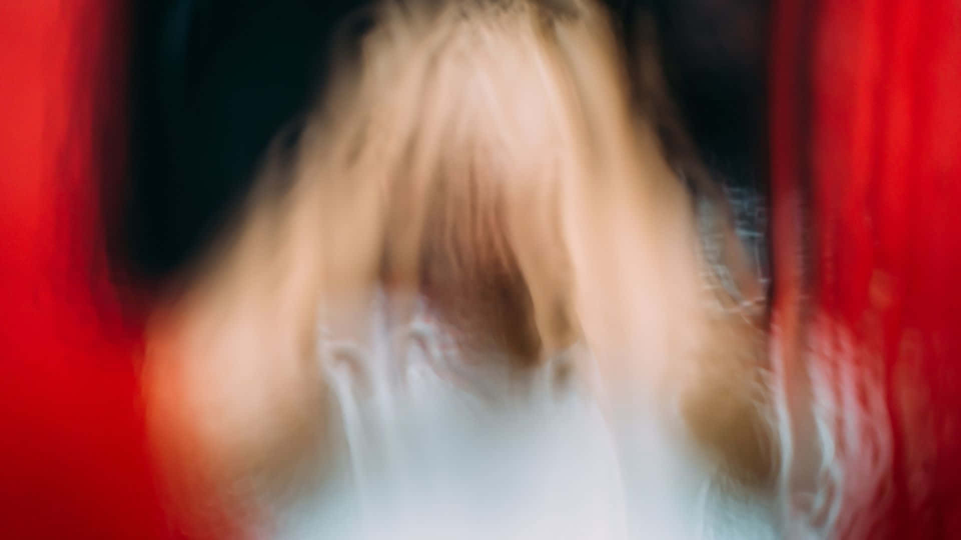  壁紙 — 一個模糊的金髮人物，身穿白色上衣，被鮮紅色的窗簾框住，營造出陰鬱的抽象構圖。