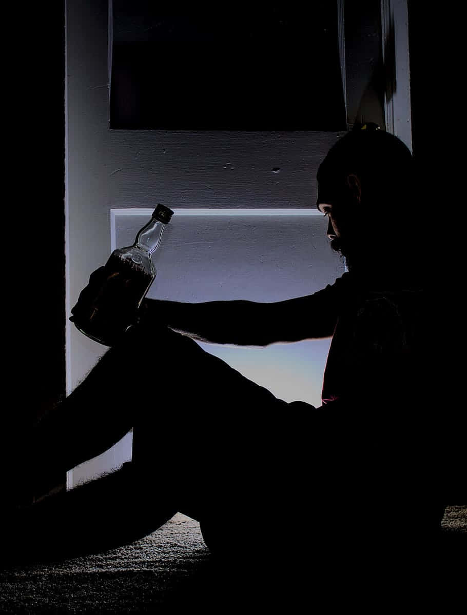  壁紙 — 一個男人坐在黑暗中，手持瓶子，背後有光線流出的剪影。