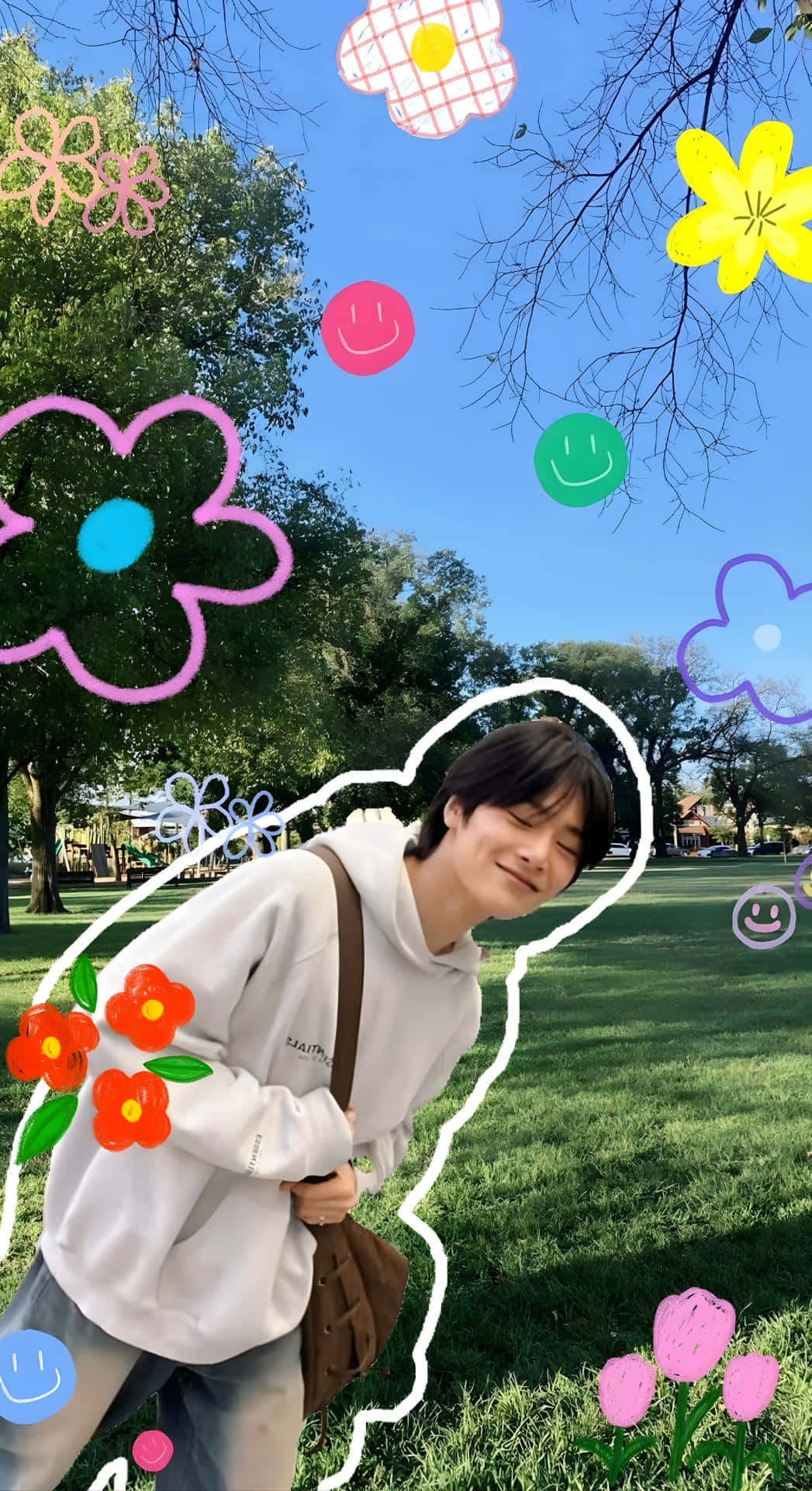  壁紙 — 一個年輕人在陽光明媚的公園裡微笑，周圍是卡通花朵和笑臉，背景是晴朗的藍天。