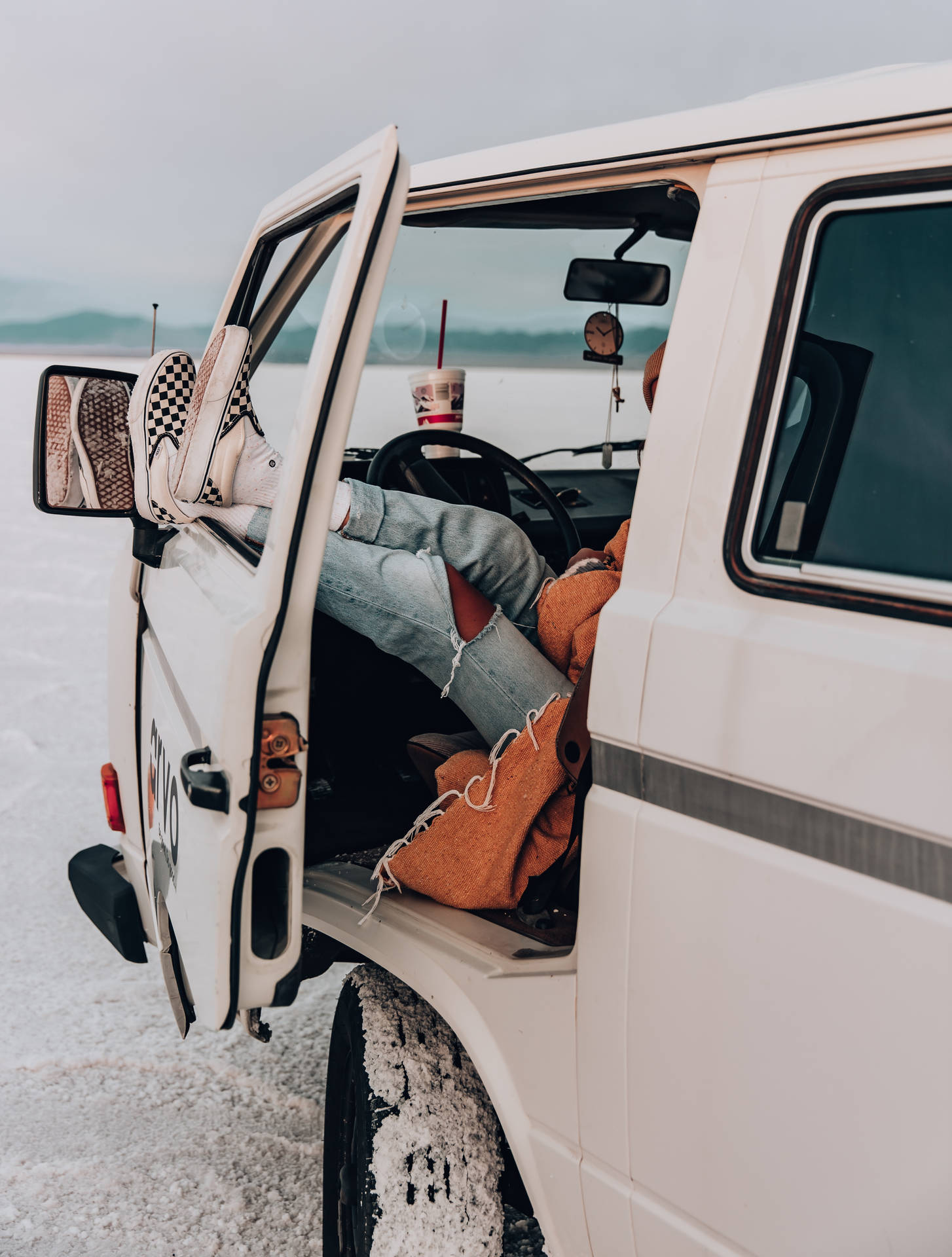 準備駕駛 Vans 鞋踏上旅程 壁紙 — 一個人在廣闊的鹽灘上，在一輛白色貨車內翹起雙腳，旁邊放著一杯咖啡。