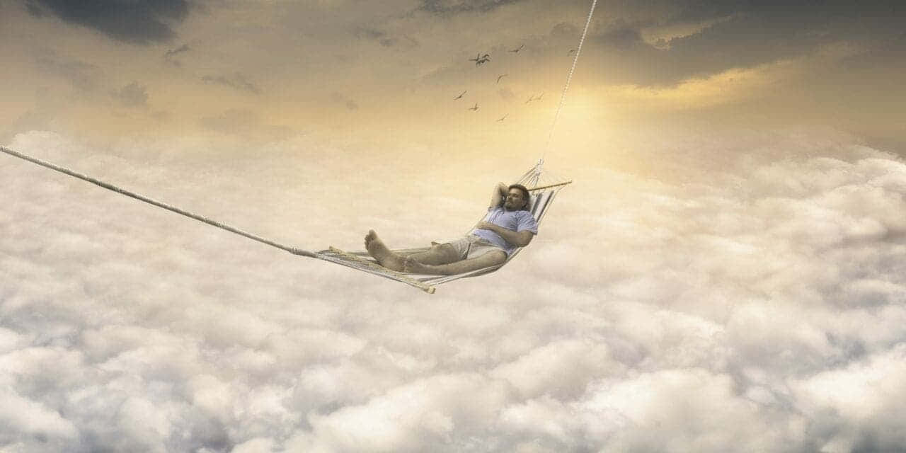  壁紙 — 一個人在金色夕陽天空下，懸掛在蓬鬆雲朵高處的吊床上休息，鳥兒在頭頂飛翔。