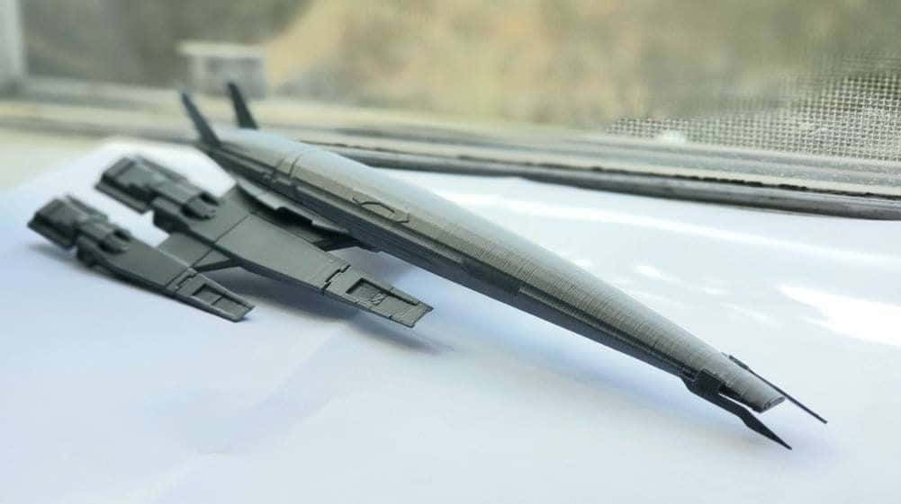 Normandy Sr-2 桌布 壁紙 — 一個時尚的黑色3D打印未來太空船模型放在白色表面上，靠近一個有模糊室外景觀的窗戶。