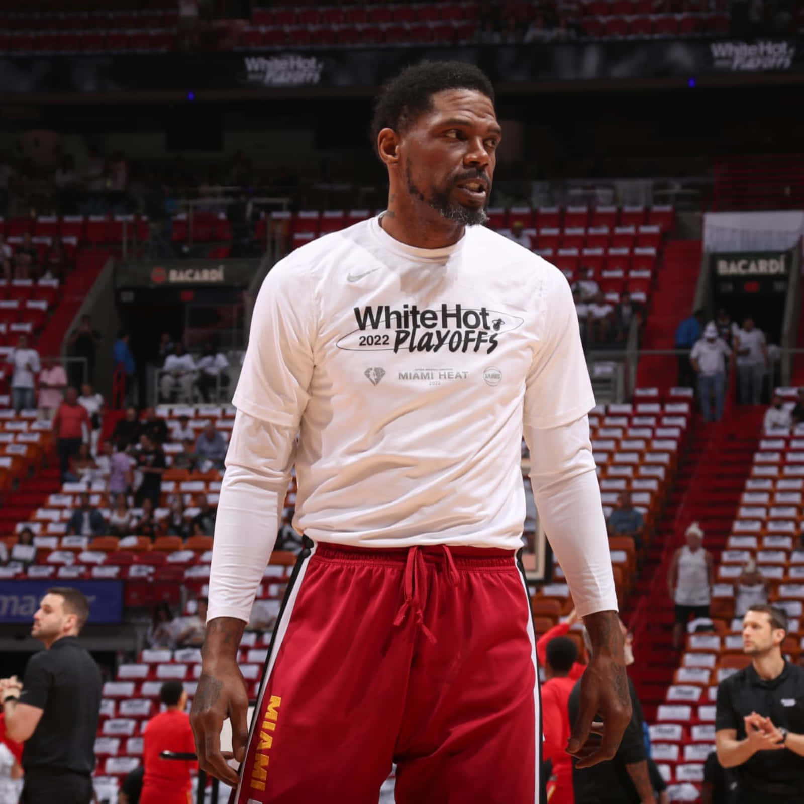  壁紙 — 一個專注的籃球運動員穿著白色 'White Hot 2022 Playoffs' 球衣和紅色邁阿密熱火短褲，站在球場上，身後是空著的紅色座位。