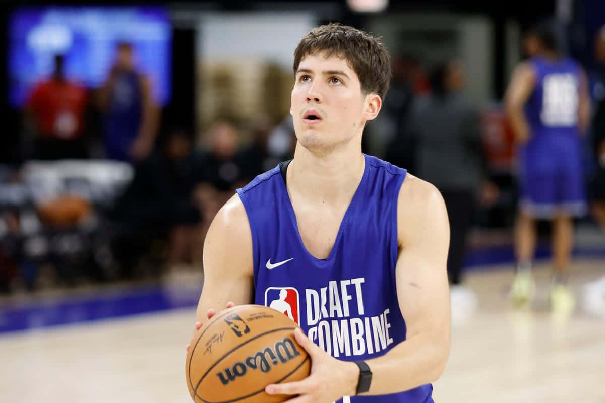  壁紙 — 一個專注的年輕籃球運動員，身穿藍色「Draft Combine」球衣，在明亮的體育館燈光下，於拋光球場上拿著威爾遜籃球。