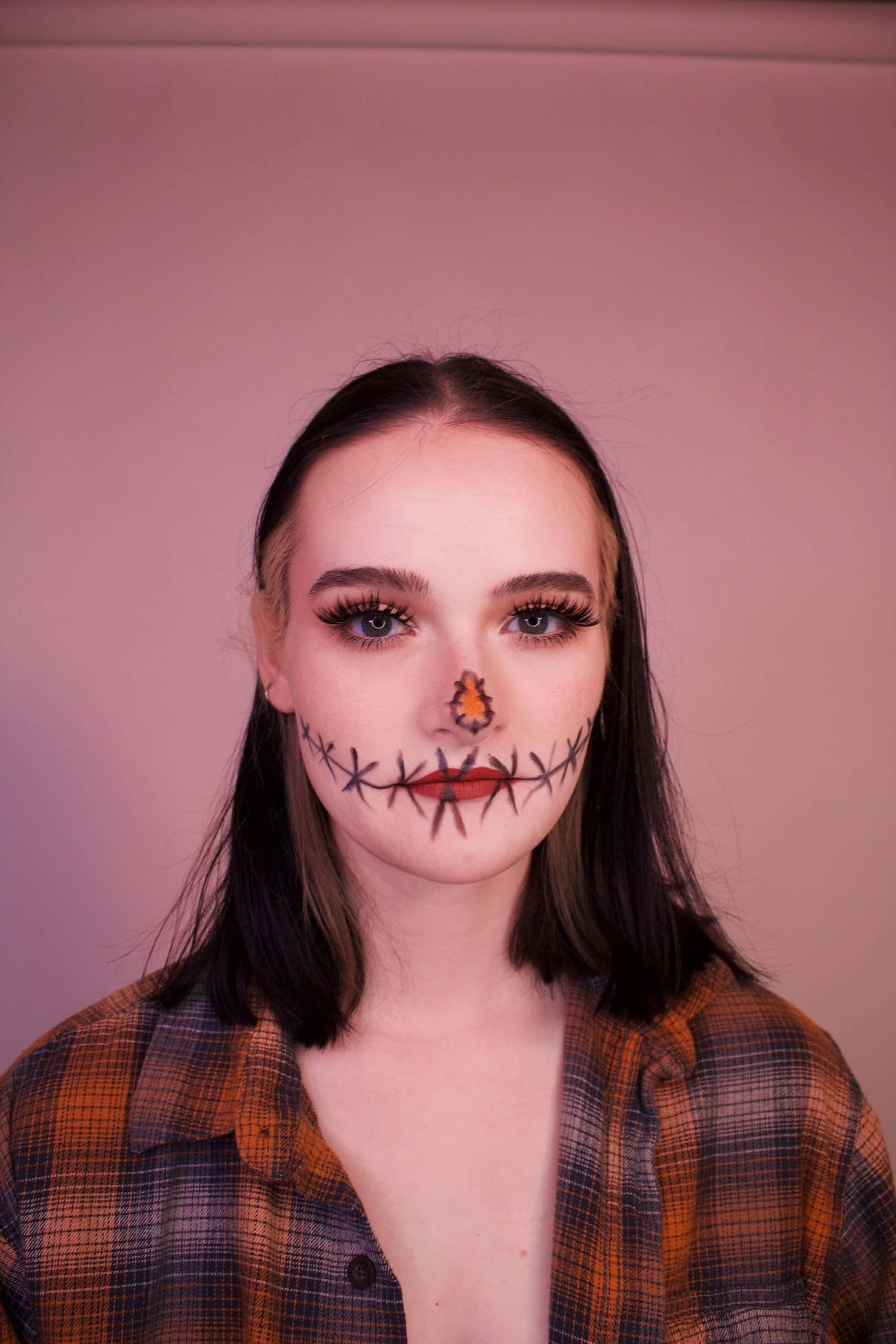 Halloween Face Paint 桌布 壁紙 — 一個嘴巴和鼻子縫合妝容的人，穿著格仔襯衫，在柔和的粉紅色背景前擺姿勢。