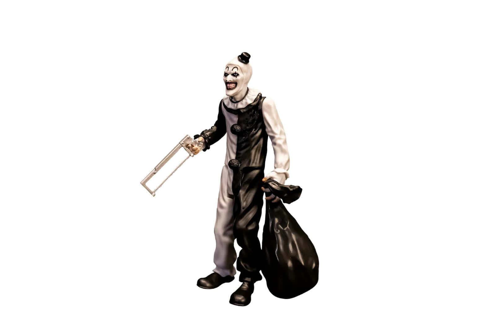  壁紙 — 一個身穿黑白服裝的可怕小丑，在純白背景前拿著一把鋼鋸和一個黑色袋子。