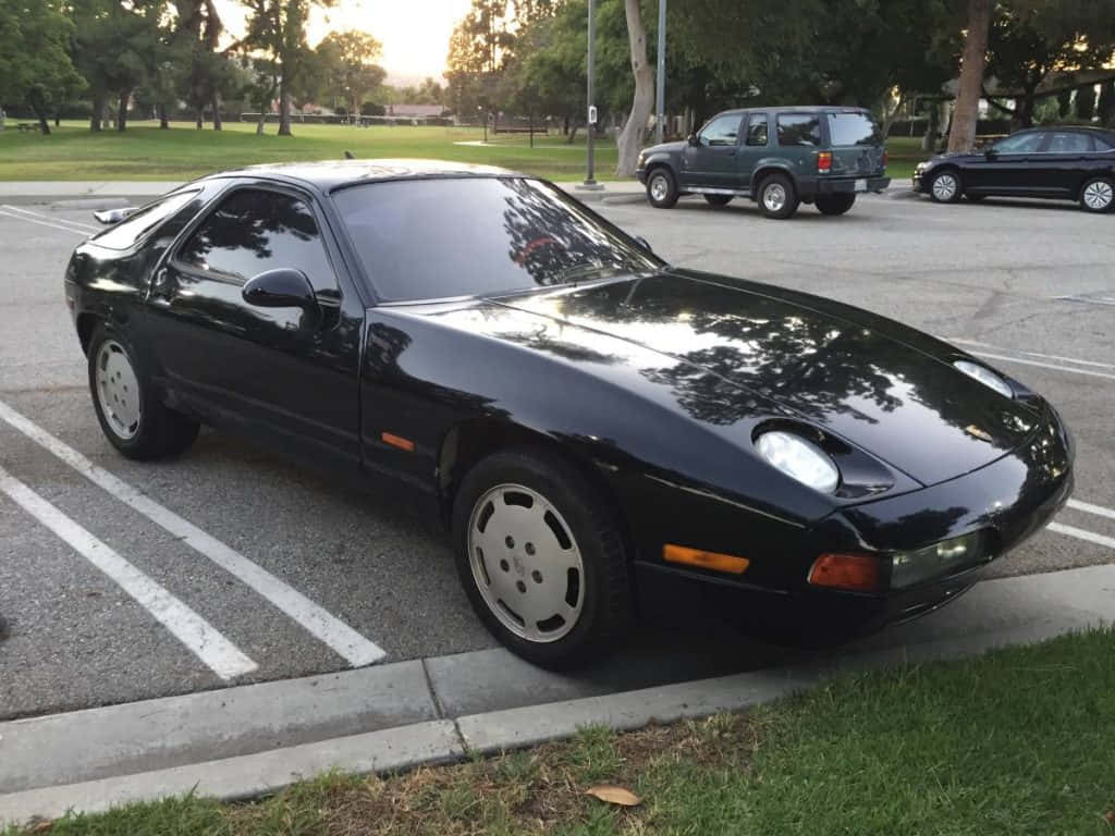 Porsche 928 桌布 壁紙 — 一架流線型的黑色保時捷928在停車場閃閃發光，黃金時段的光線反射在其拋光表面上。