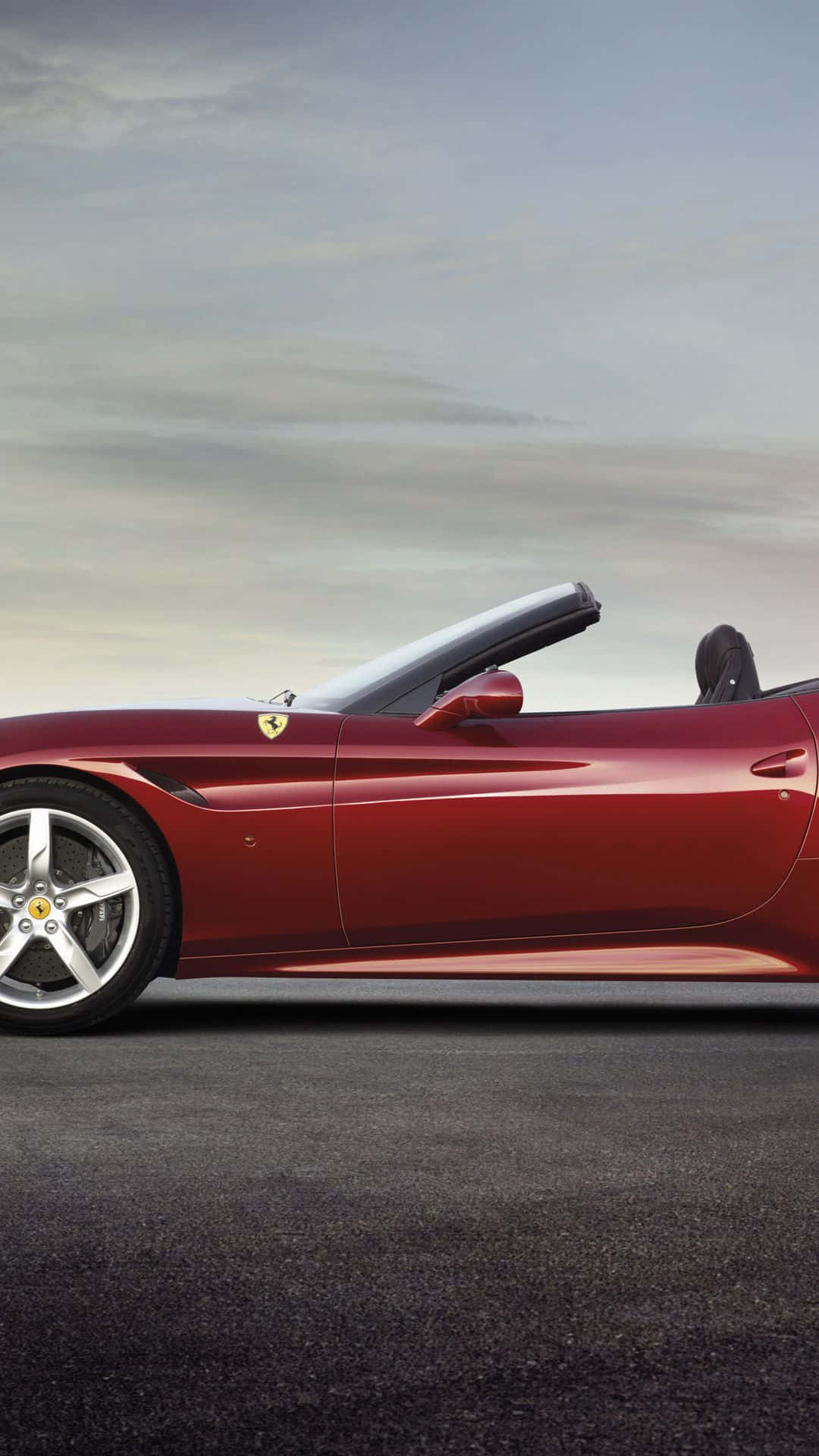 Ferrari California T 桌布 壁紙 — 一架時尚的紅色法拉利開篷車停泊在瀝青路上，天空柔和灰色帶有雲朵。