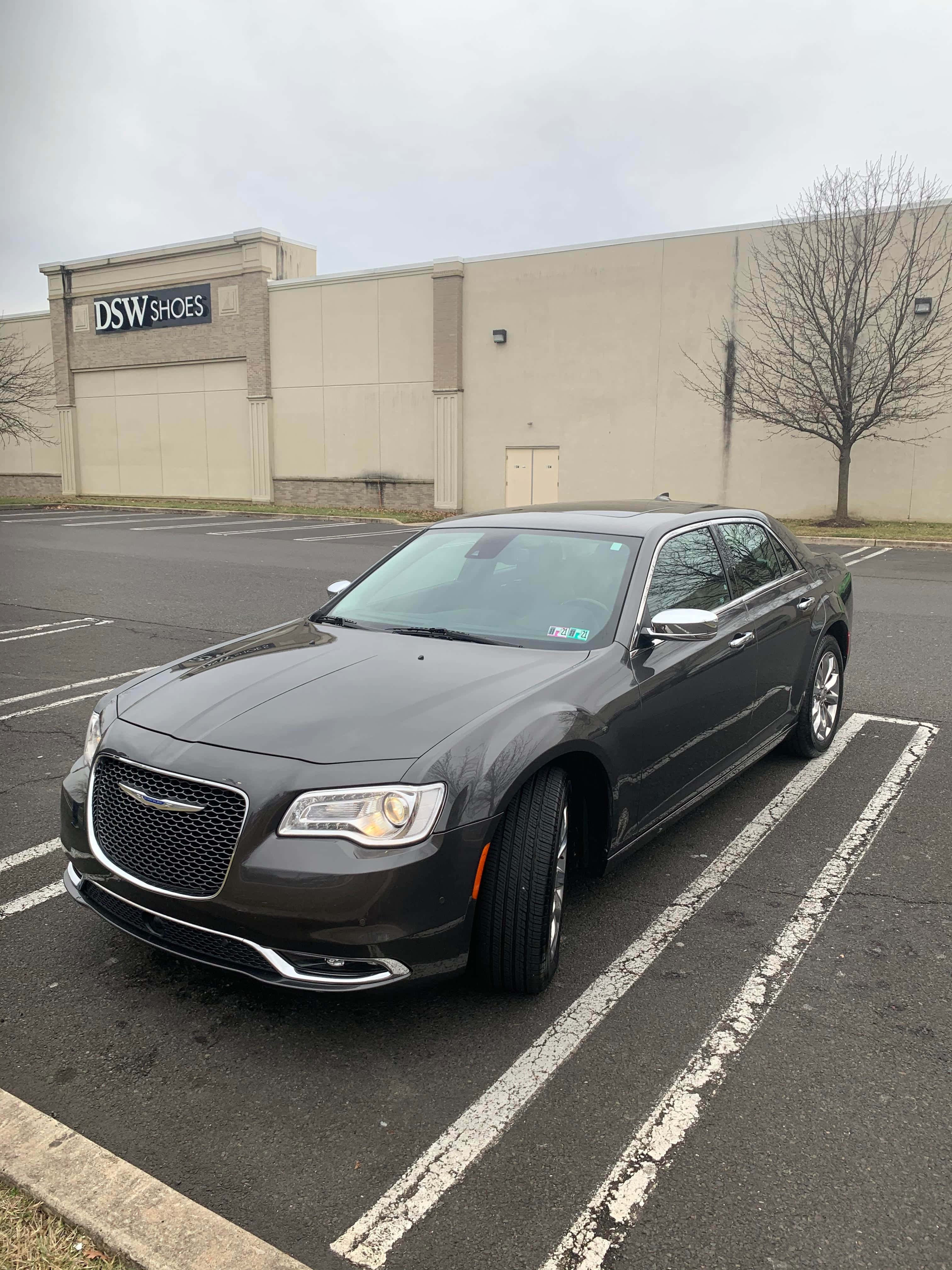 Chrysler 300 桌布 壁紙 — 一架時尚的深灰色克萊斯勒轎車停在濕漉漉的停車場，背景是DSW Shoes商店，天空多雲。