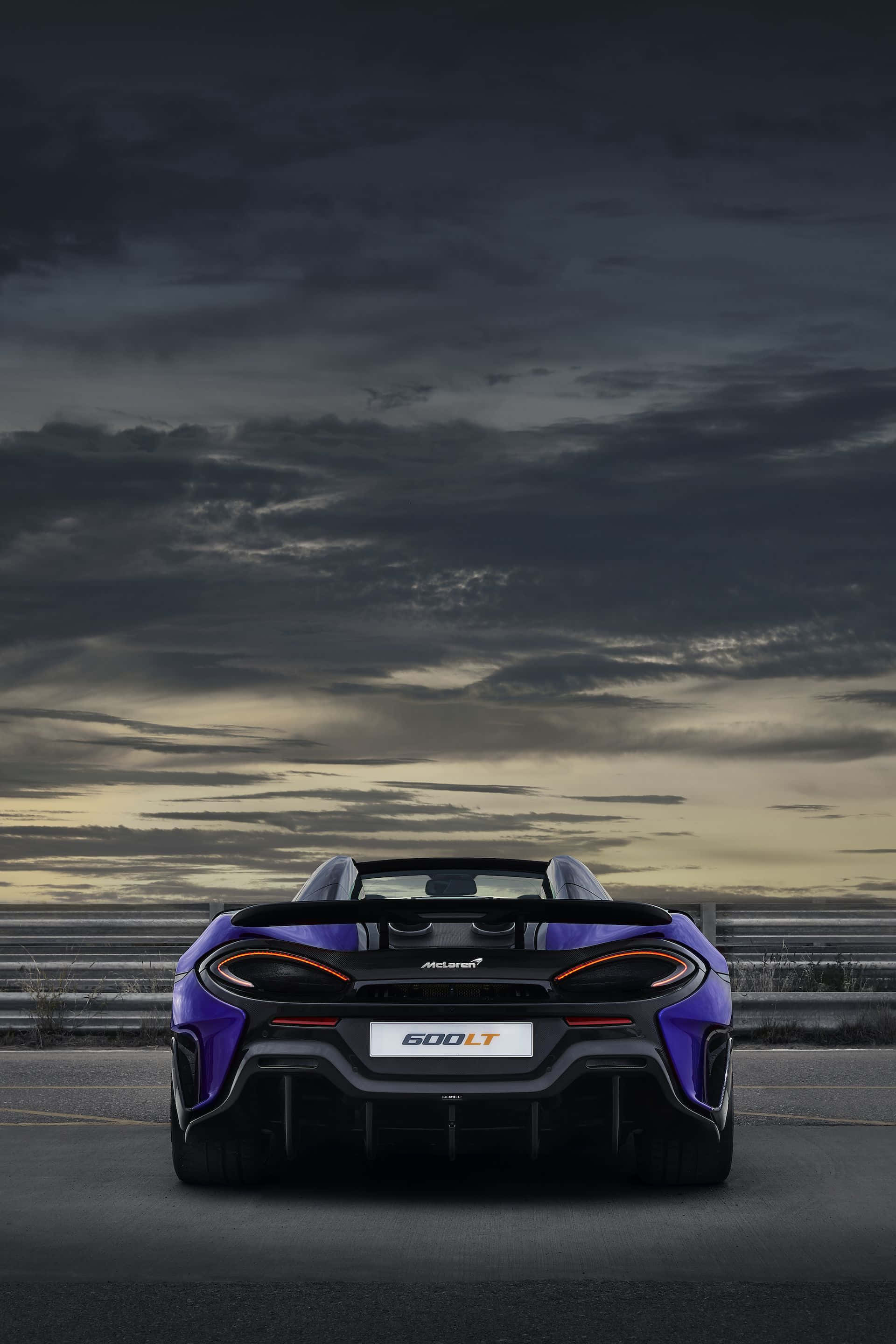 Mclaren 600lt 桌布 壁紙 — 一架充滿活力的紫色McLaren 600LT跑車，在戲劇性的暮色天空下從後方觀看賽道。