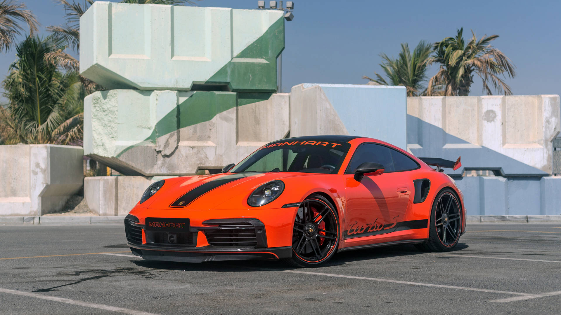 橙色Manhart保時捷911 Turbo S停泊在混凝土塊和棕櫚樹附近。