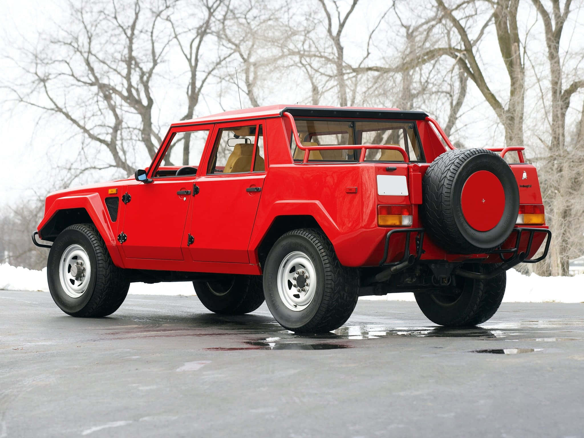 Lamborghini Lm002 桌布 壁紙 — 一架搶眼的紅色林寶堅尼LM002停泊在濕漉漉的路面上，周圍是灑滿白雪的禿樹。