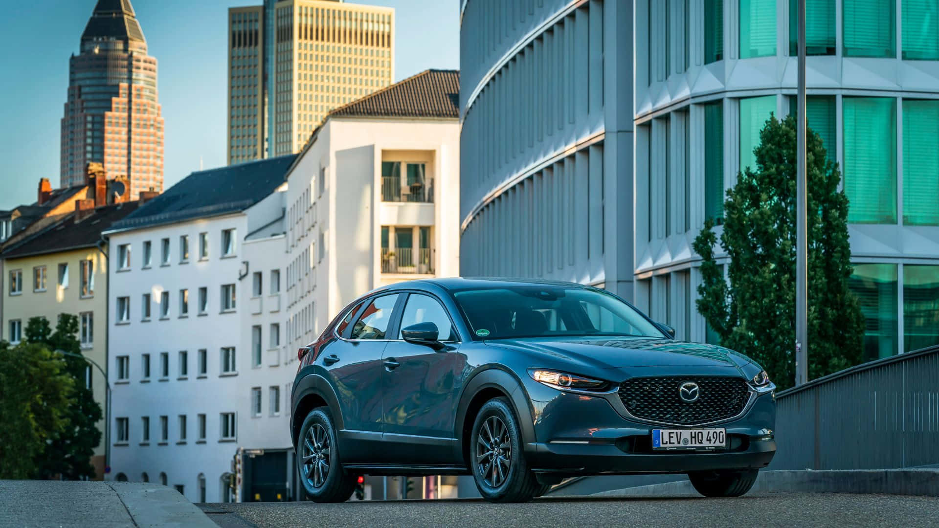 Mazda Cx-3 桌布 壁紙 — 一輛時尚的深藍色Mazda CX-3停泊在現代與歷史建築交錯的城市街道上，天空晴朗。