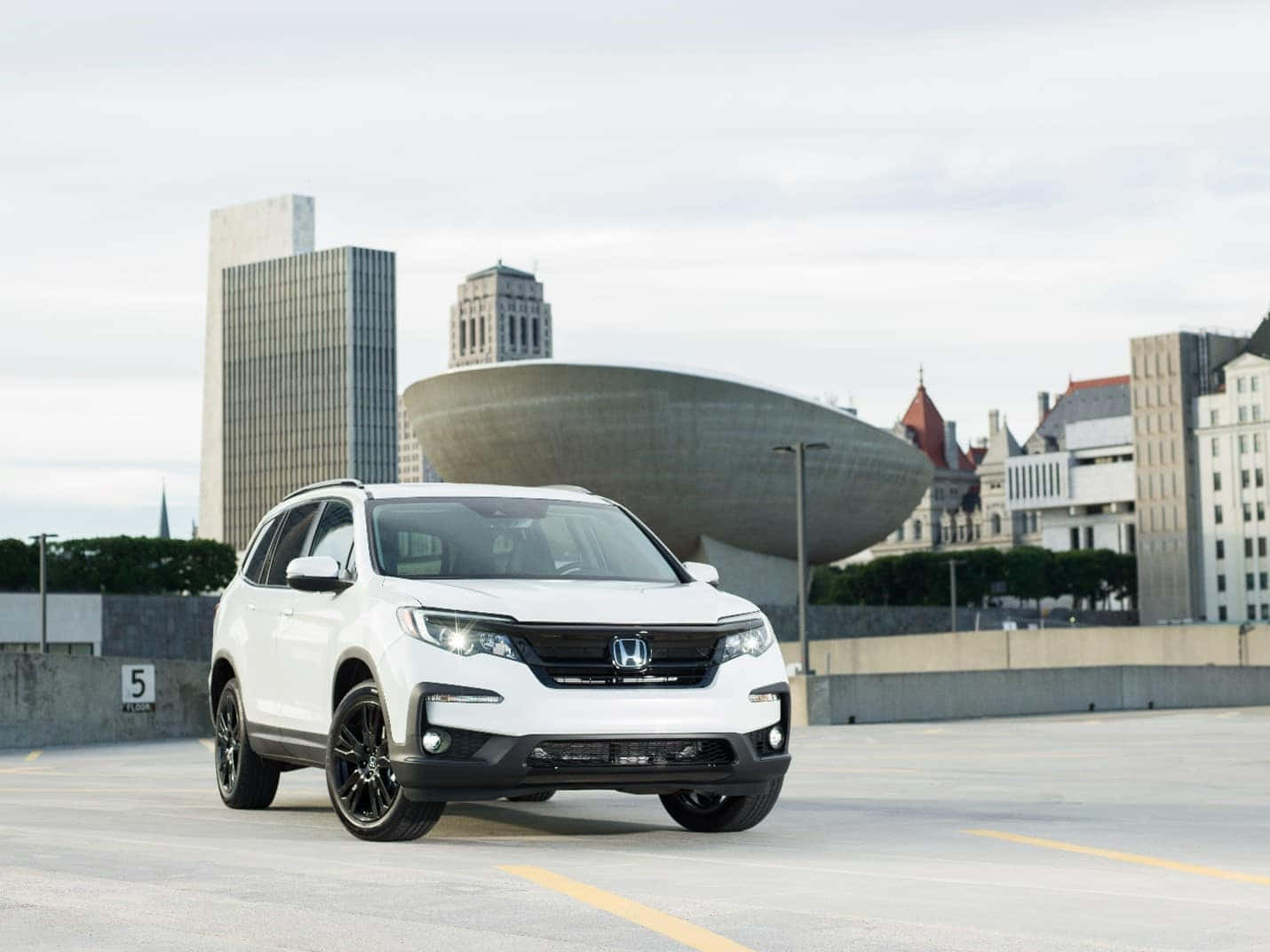 Honda Pilot 桌布 壁紙 — 一輛白色本田SUV配黑色輪圈，停泊在現代建築背景的城市停車場。