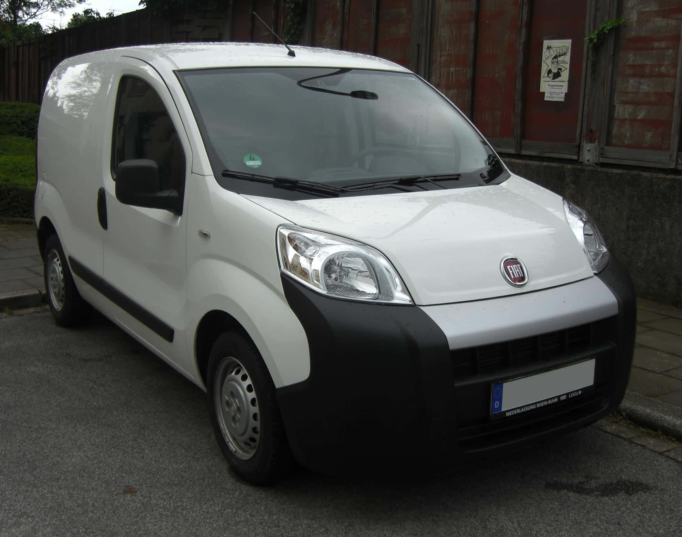 Fiat Fiorino 桌布 壁紙 — 一輛白色Fiat客貨車停泊在鋪砌的街道上，旁邊是風化的紅色木柵欄。