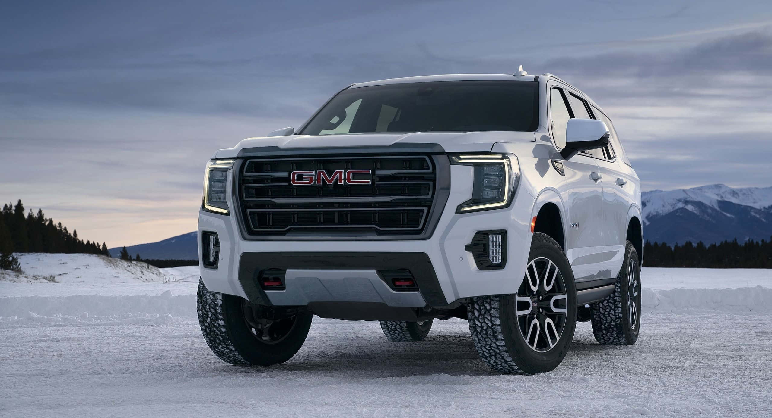 Gmc Yukon 桌布 壁紙 — 一輛白色GMC SUV大膽地矗立在雪地上，背景是白雪覆蓋的山脈和暮色天空。