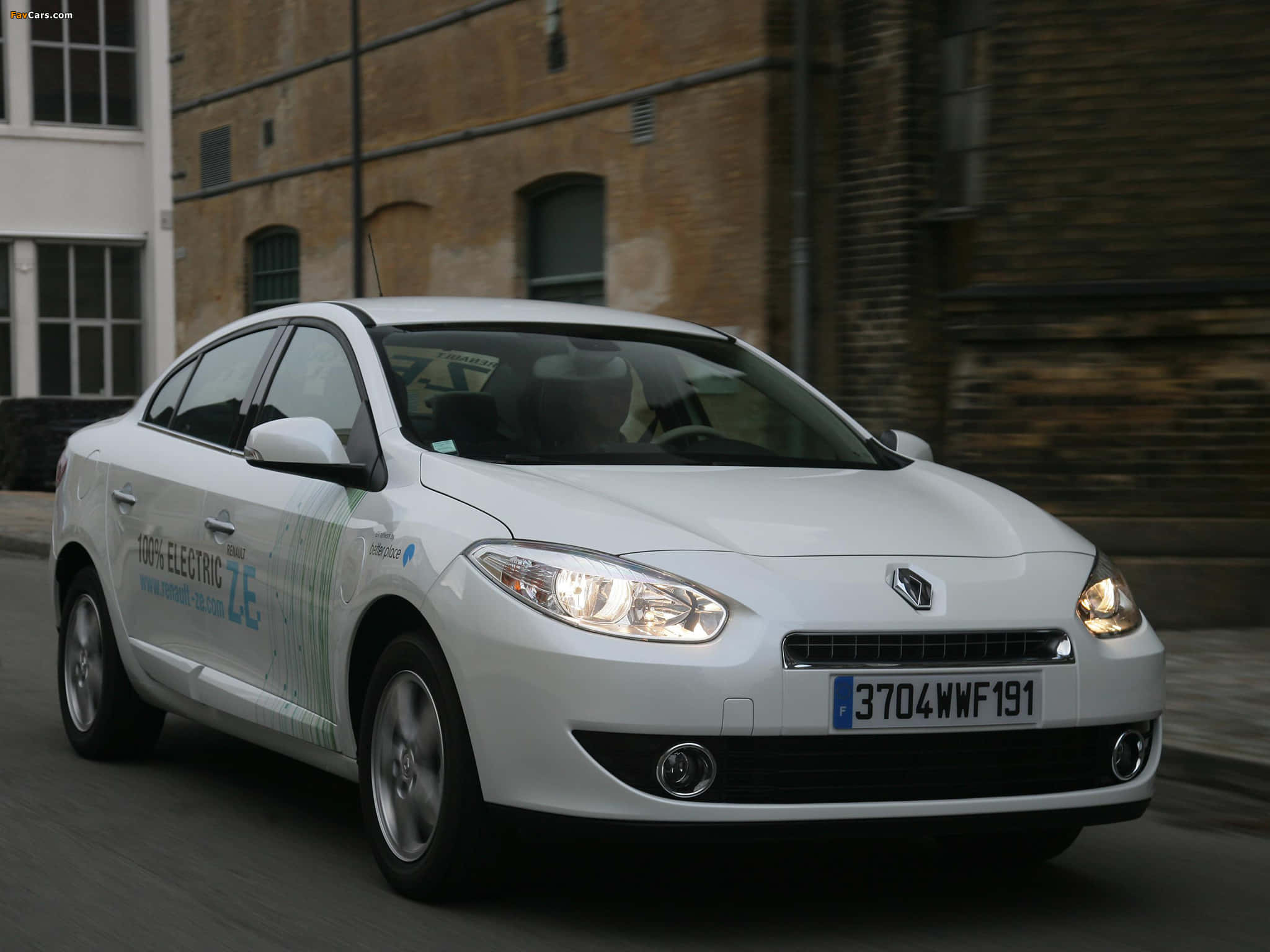 Renault Fluence 桌布 壁紙 — 一輛白色雷諾Zoe電動車在街上駛過磚砌建築，帶有動態模糊效果。