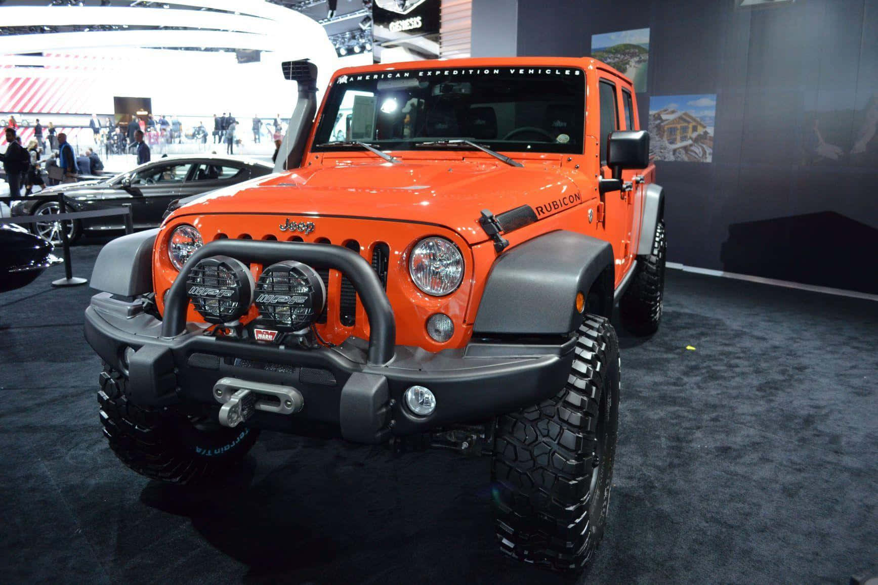 Jeep Gladiator 桌布 壁紙 — 一輛充滿活力的橙色Jeep Wrangler Rubicon配備黑色越野裝備，在深色地毯地板的車展上展出。