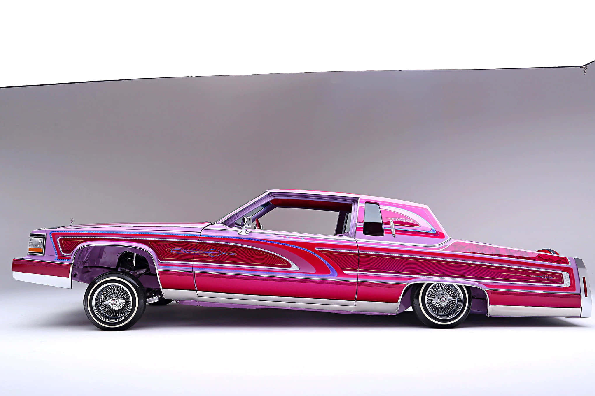 Cadillac Fleetwood 桌布 壁紙 — 一輛充滿活力的粉紅色和紫色定制低底盤汽車，帶有鍍鉻細節和流暢的油漆工作，在工作室背景下以側面展示。