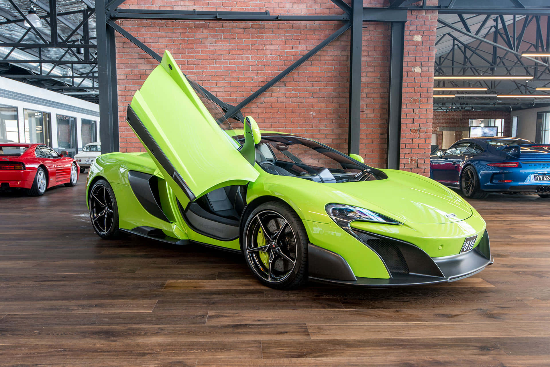Mclaren 675lt Spider 桌布 壁紙 — 一輛充滿活力的青檸綠色McLaren跑車，打開蝴蝶門，在磚和鋼的質樸展廳中，在明亮的燈光下閃閃發光。
