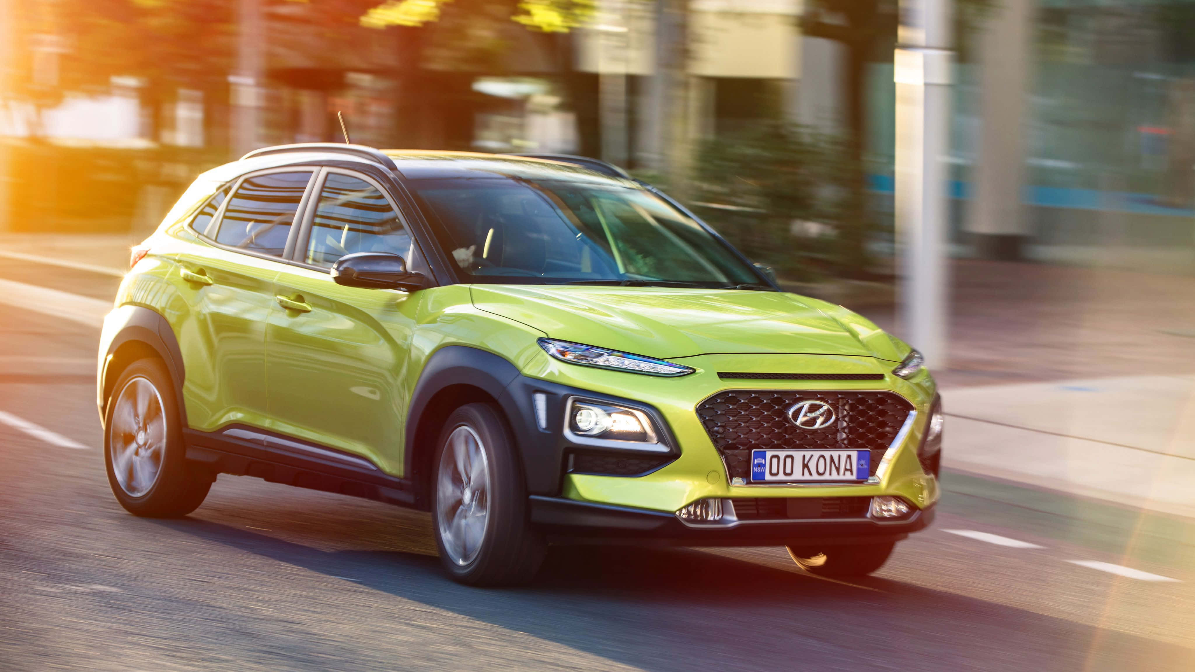 Hyundai Kona 桌布 壁紙 — 一輛充滿活力的青檸綠色現代Kona SUV在陽光明媚的城市街道上疾馳，背景呈現動態模糊效果。