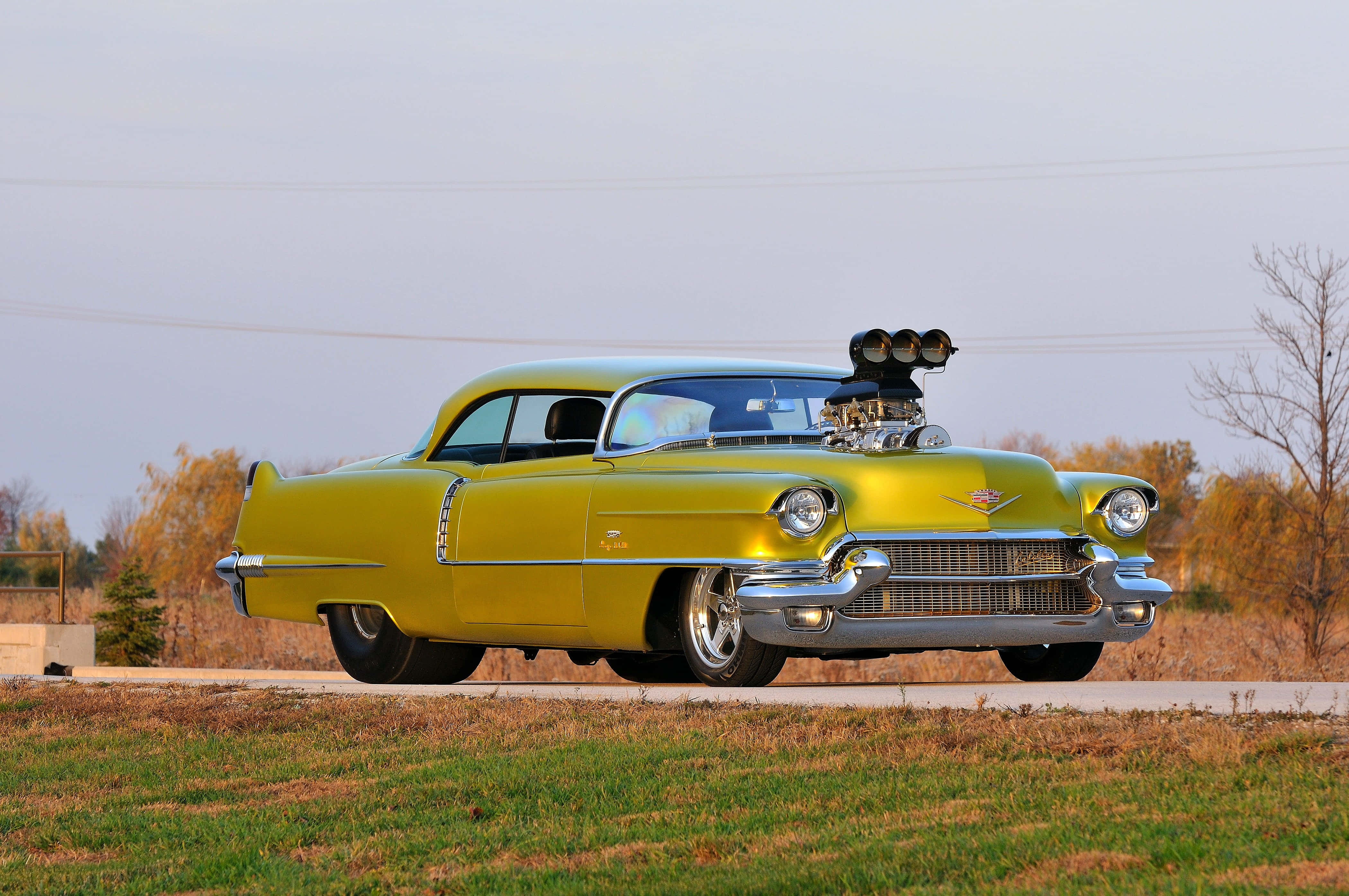 Cadillac Deville 桌布 壁紙 — 一輛充滿活力的黃色經典汽車，帶有鍍鉻增壓器，停在秋天的路邊。